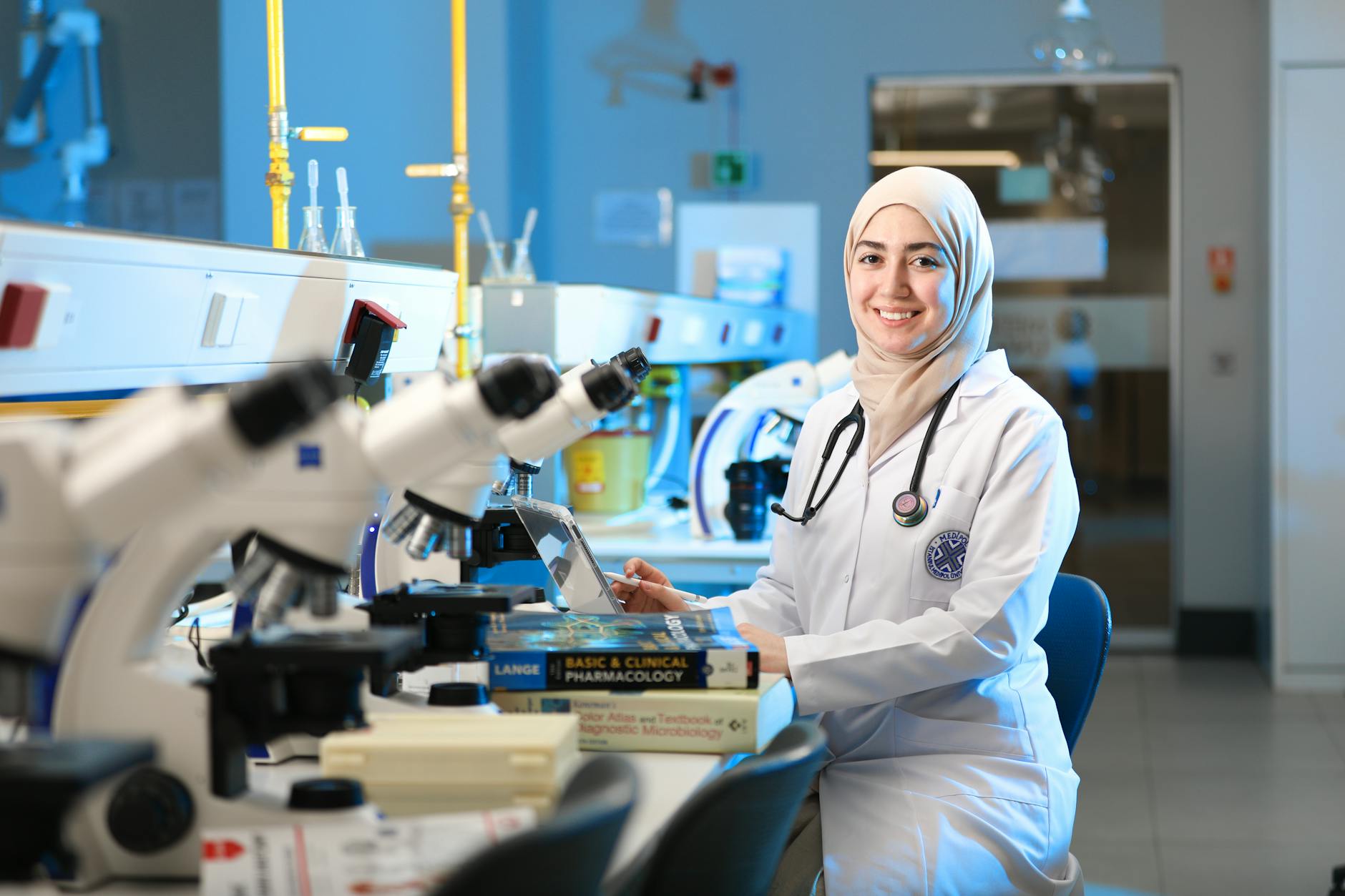 farmaco Parkinson da plastica — A confident female scientist in a lab coat with a hijab in a modern laboratory with microscopes and textbooks.