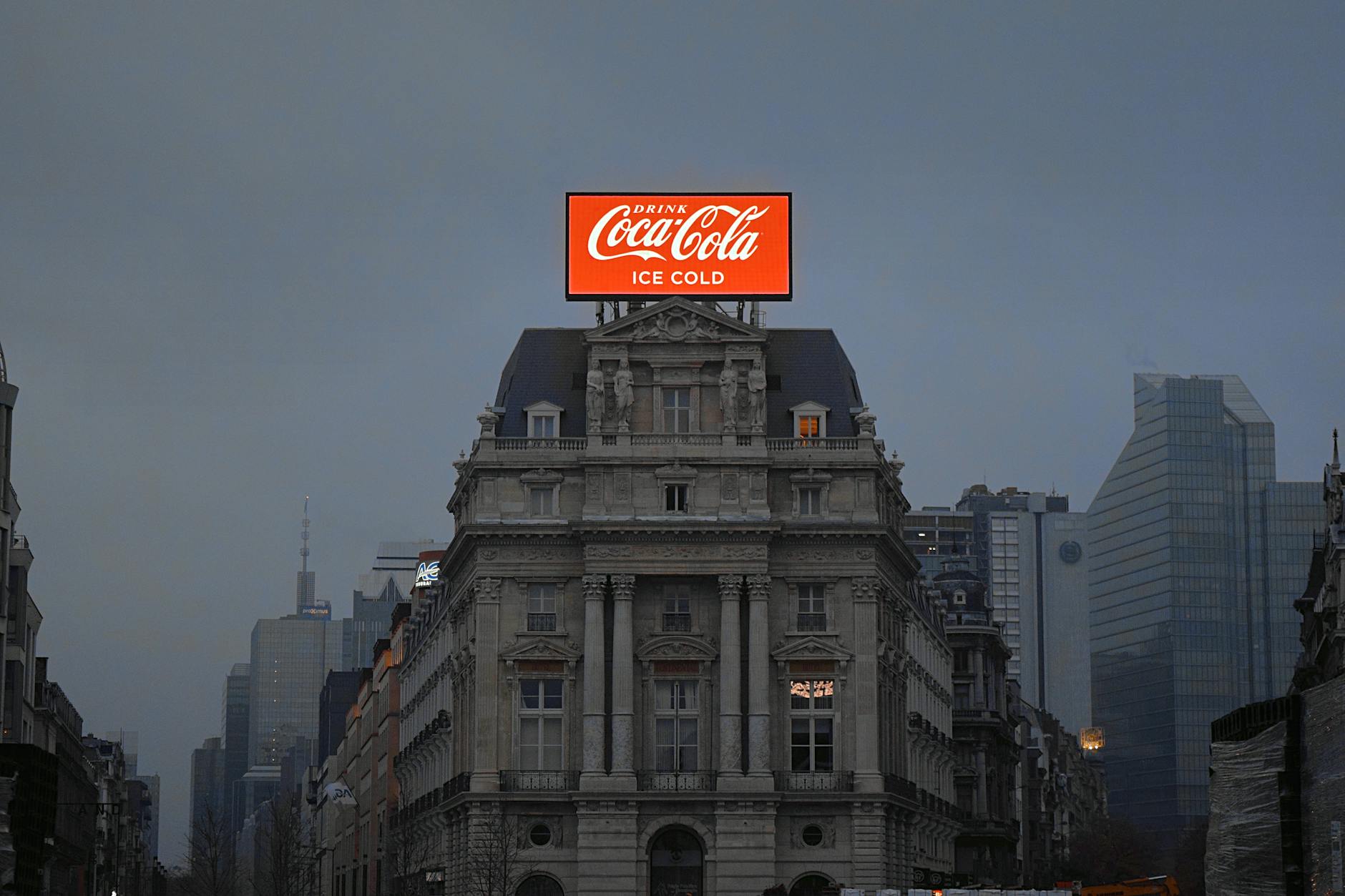 strategia energetica europea — Coca-Cola billboard atop historic architecture in Brussels during twilight.