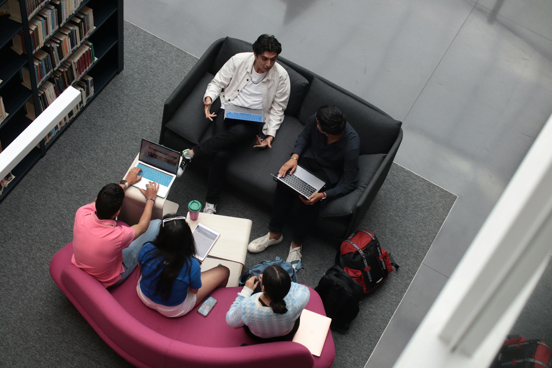 incontri al Circolo dei lettori — A group of diverse students using laptops and books in a library setting, studying together.
