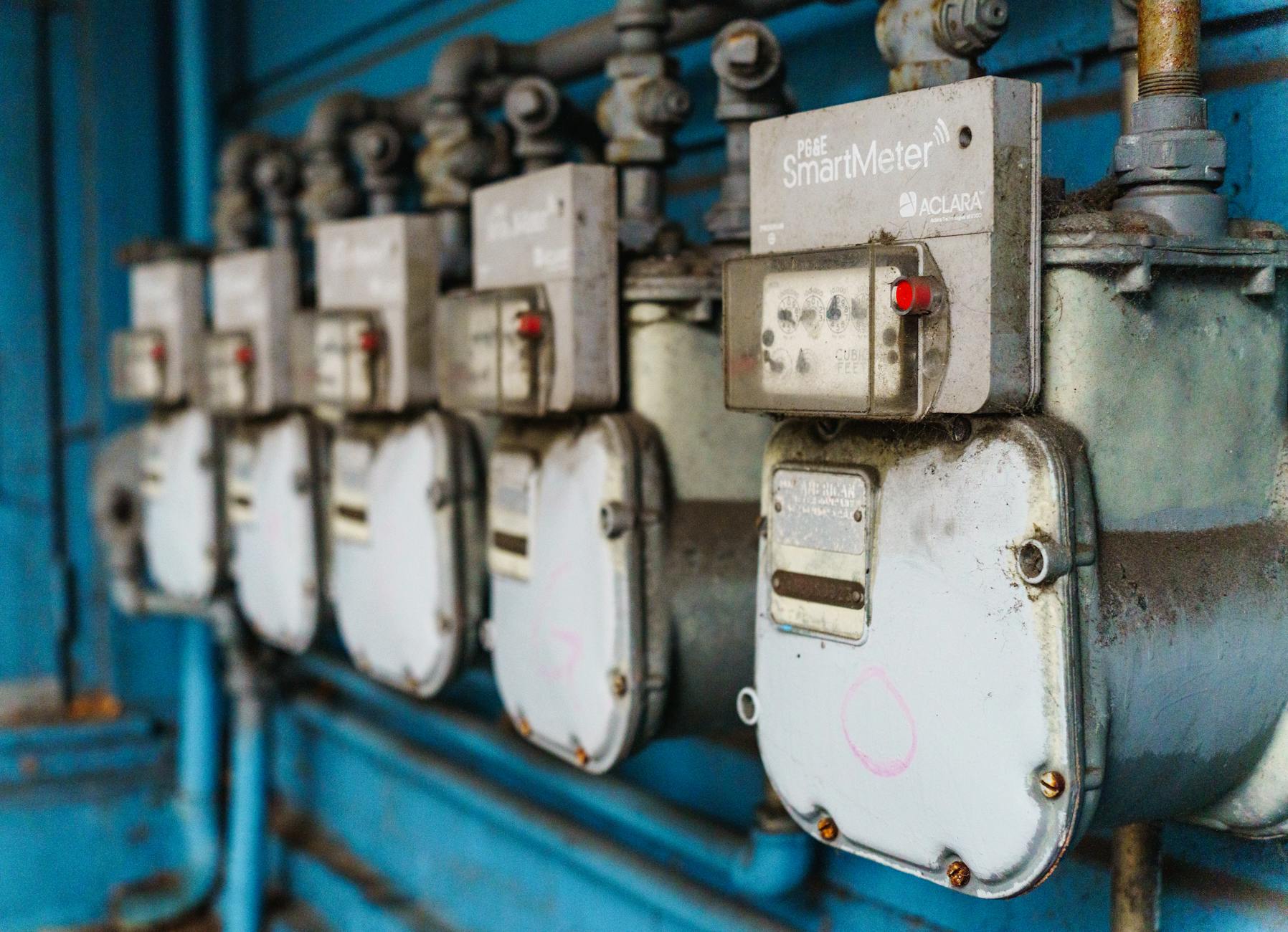 piano energia UE — Multiple smart utility meters lined up on a blue industrial wall.