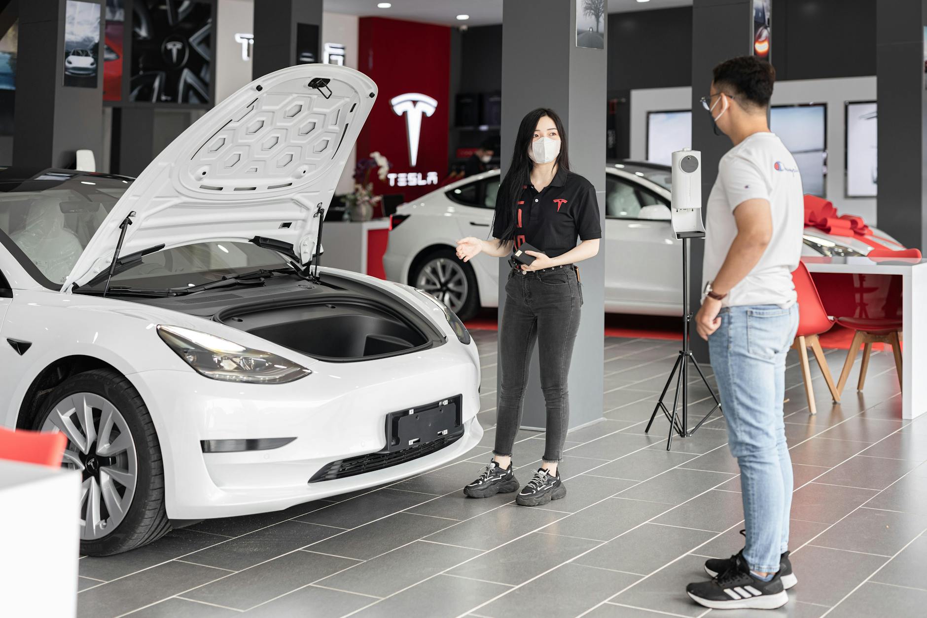 incentivi auto elettriche — A customer talks with a sales representative about a Tesla Model 3 in a car dealership, showcasing the electric car's features.