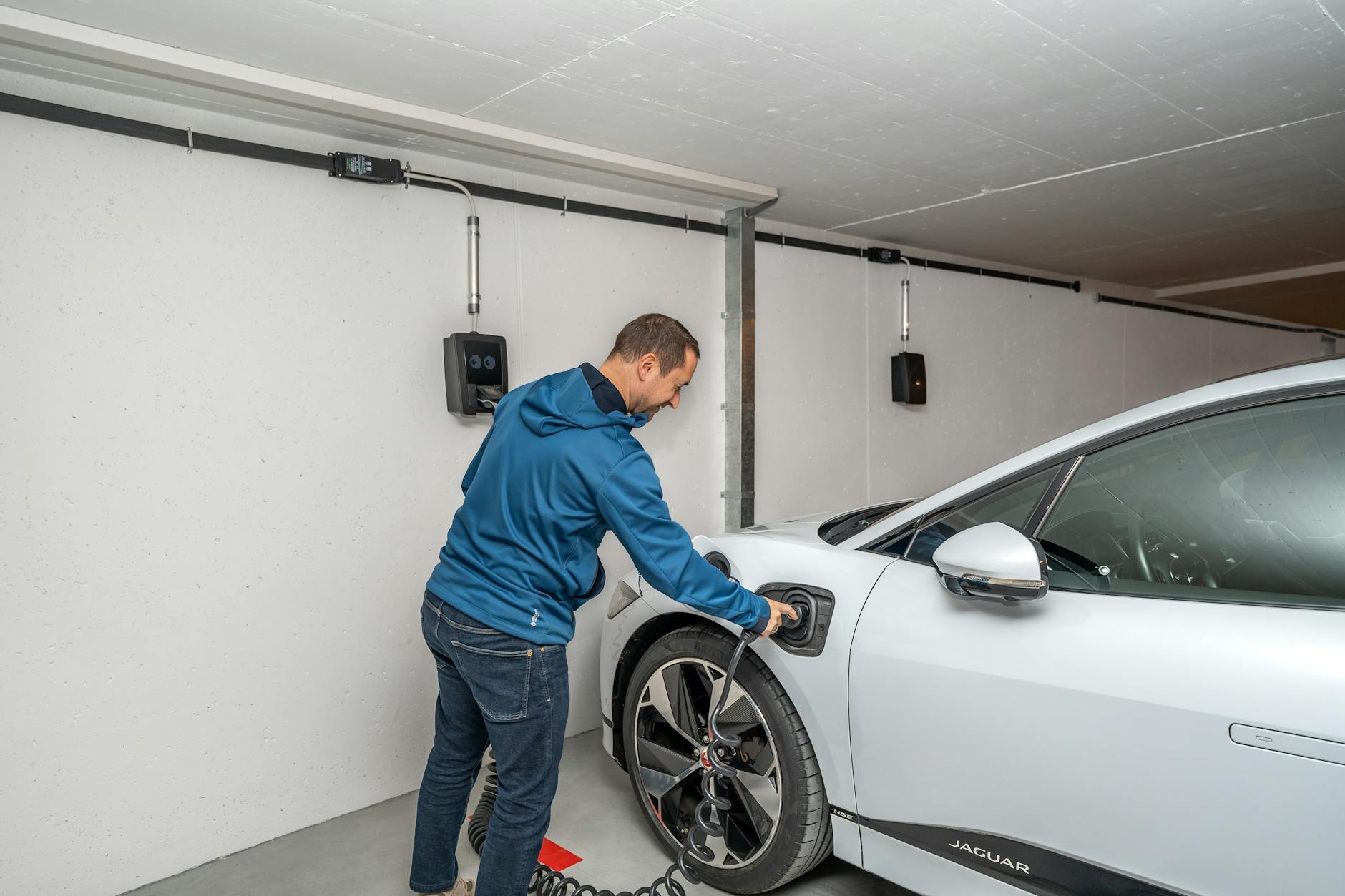 incentivi moto elettriche 2026 — A man connects an electric car to a charging station in a modern indoor garage setting.