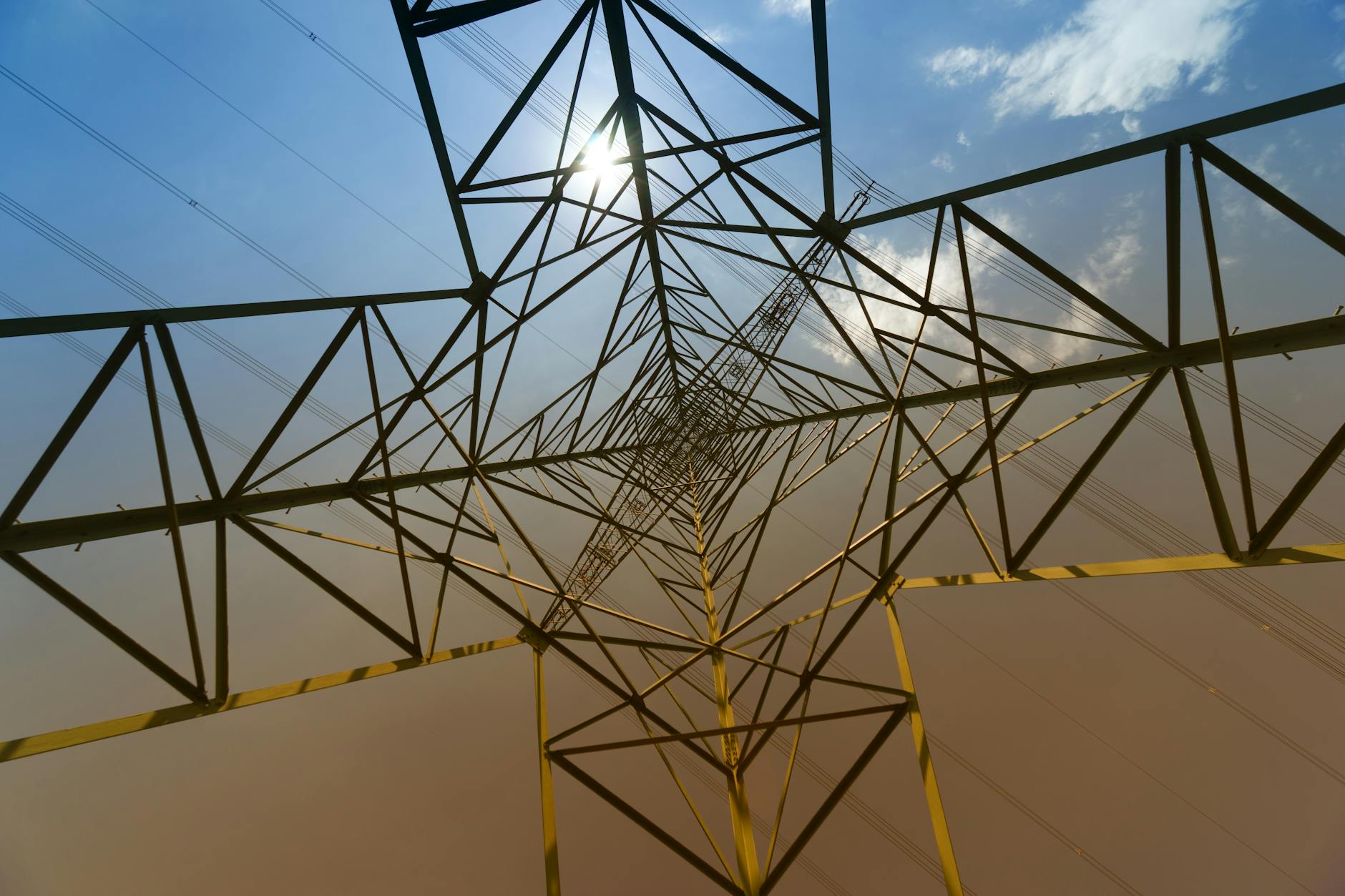 misure nazionali urgenti — Looking up view of a steel transmission tower with sun glare and blue sky.