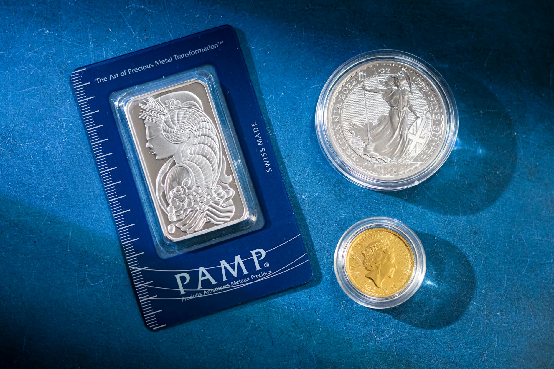 metalli preziosi — Silver bar and coins on blue surface, highlighting investment and collectible value.