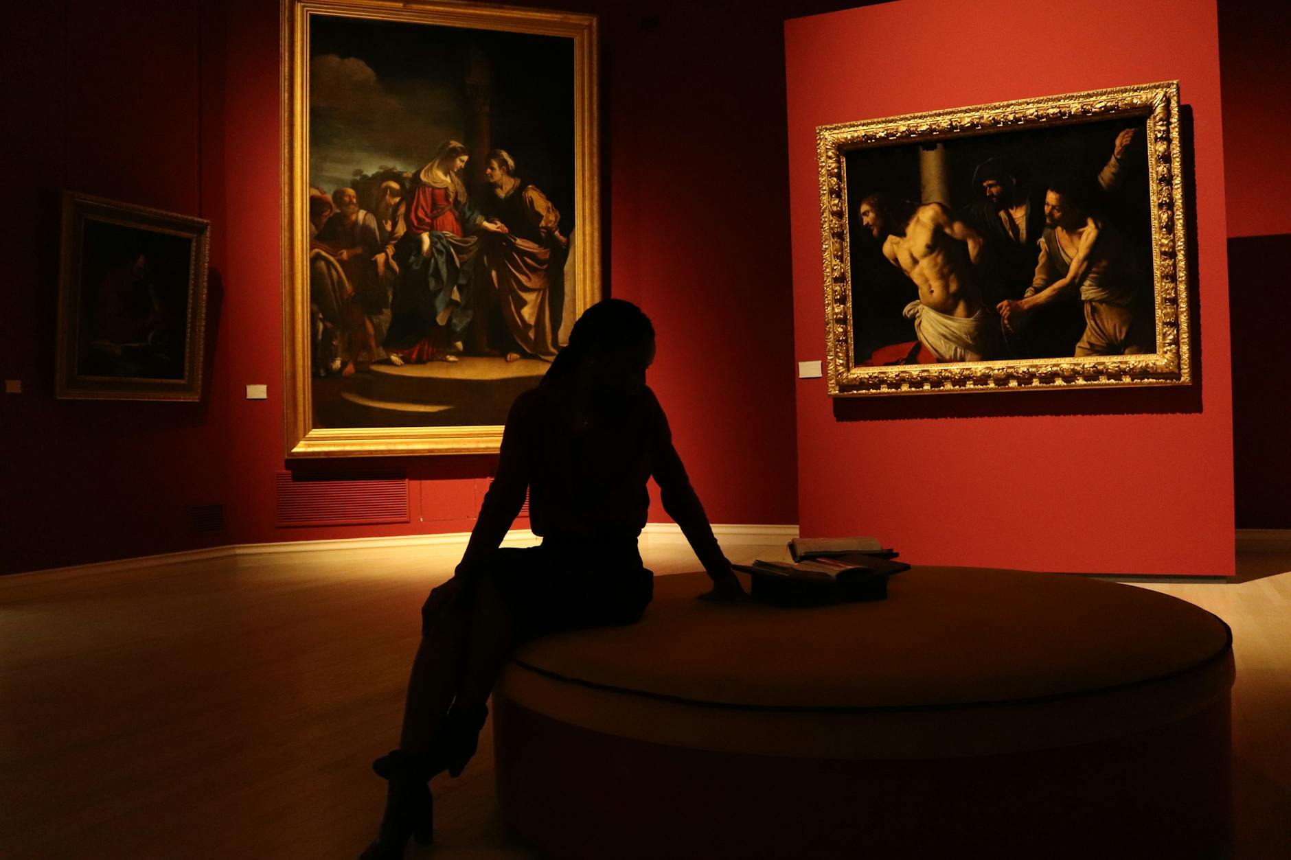 Milano ArtWeek — Silhouetted visitor in an art gallery with dramatic lighting on classic paintings.