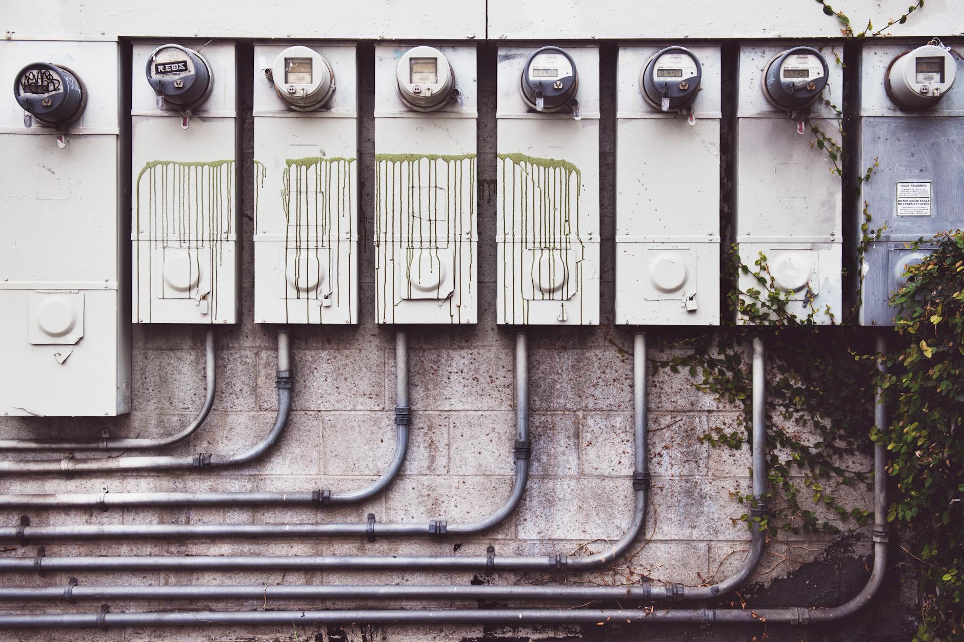 risparmio bolletta elettrica — Array of outdoor electric meters on a brick wall with vines.