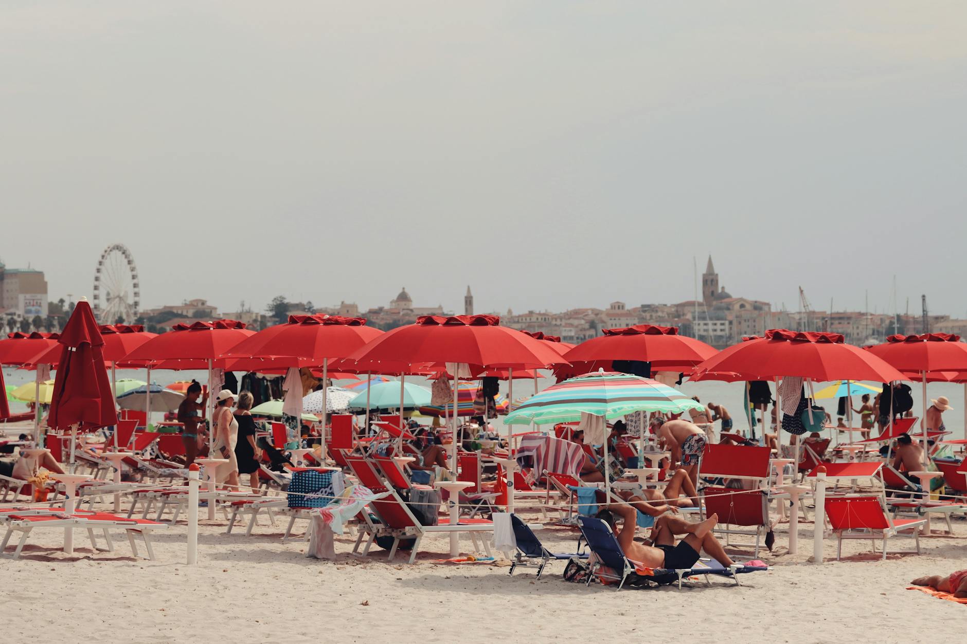 turismo estivo — Tourists enjoy the sunny day under red umbrellas at Alghero Beach, Sardinia, Italy.