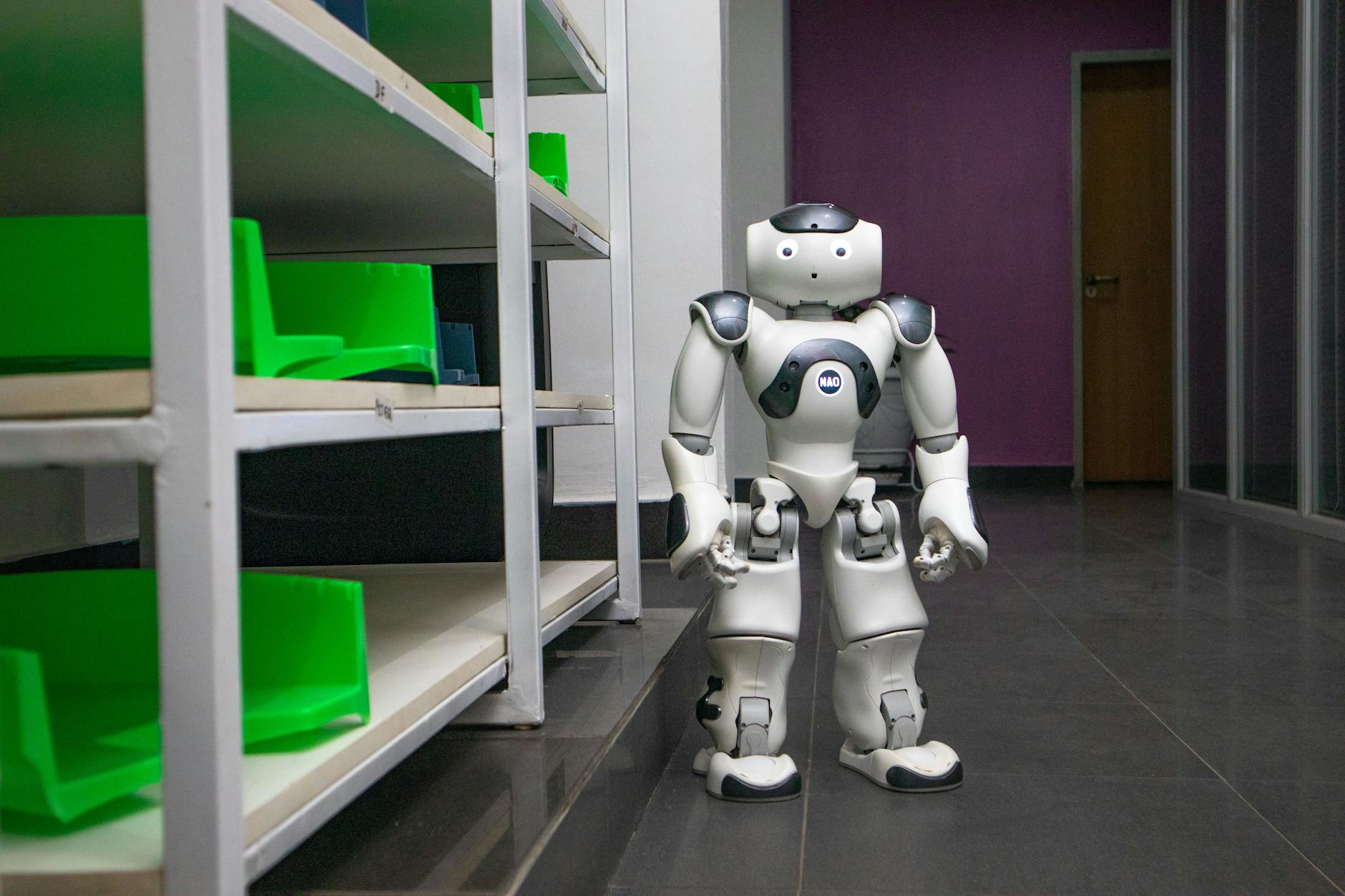 robot umanoidi nelle scuole — A humanoid robot standing in a modern corridor with shelves, representing futuristic technology.