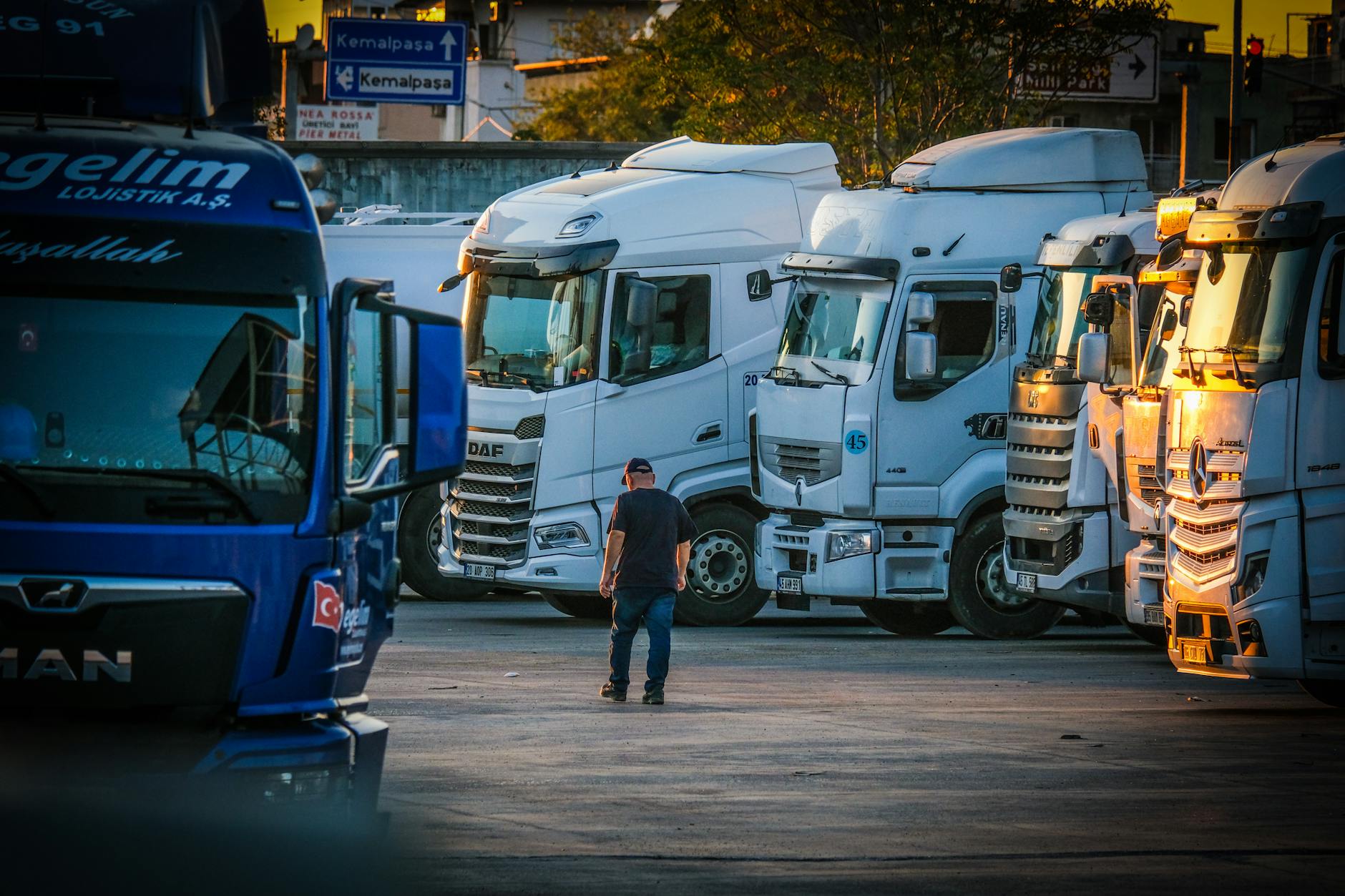 protesta autotrasportatori — A man walks among parked trucks at sunset in an industrial area, creating a serene yet busy scene.
