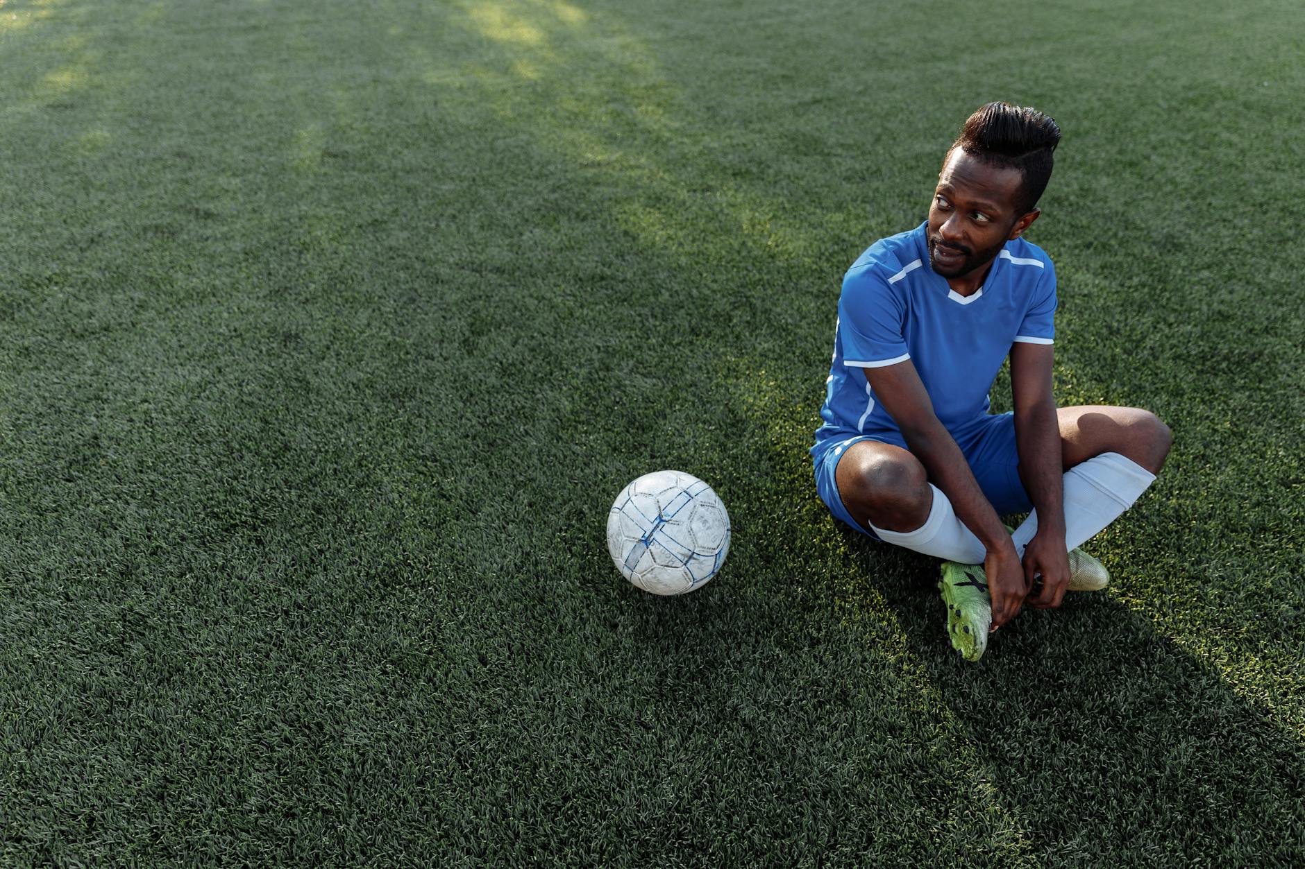 nazionale italiana esclusa Mondiali — A soccer player in a blue jersey sits on the grass field during the day.