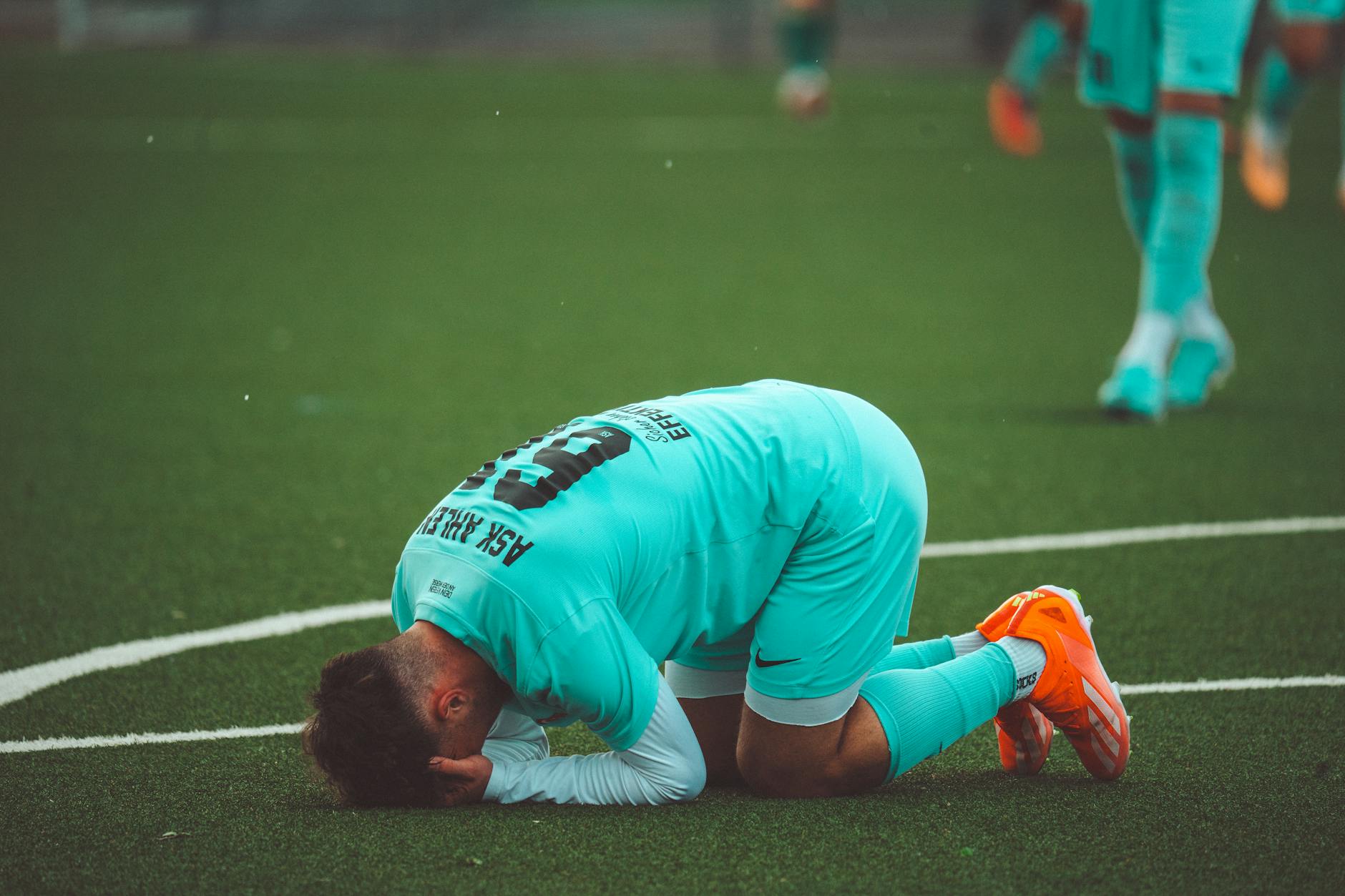 Italia fuori dai Mondiali — A soccer player kneels in despair on a green artificial turf sports field.