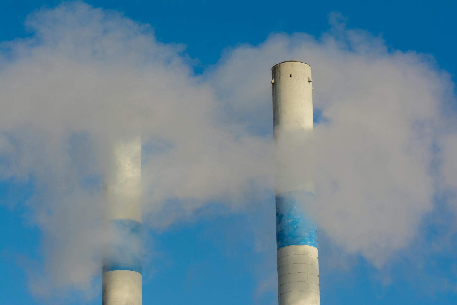 modifiche sistema ETS — Twin industrial chimneys emitting smoke under a clear blue sky, highlighting air pollution concerns.