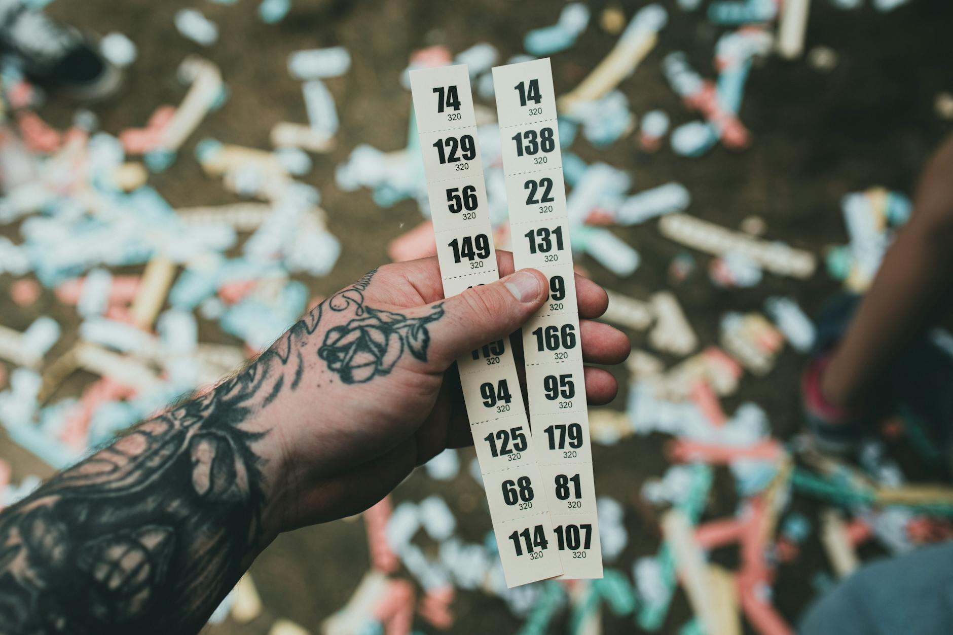 numeri estratti Lotto — Close-up of a tattooed hand holding raffle tickets amidst confetti at a festival setting.