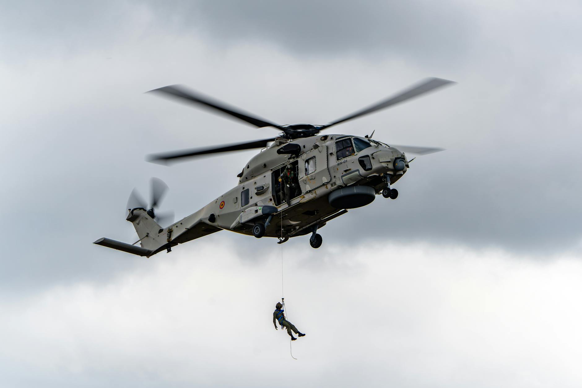 aviatore americano liberato — A military helicopter in flight during a rope operation in the sky.