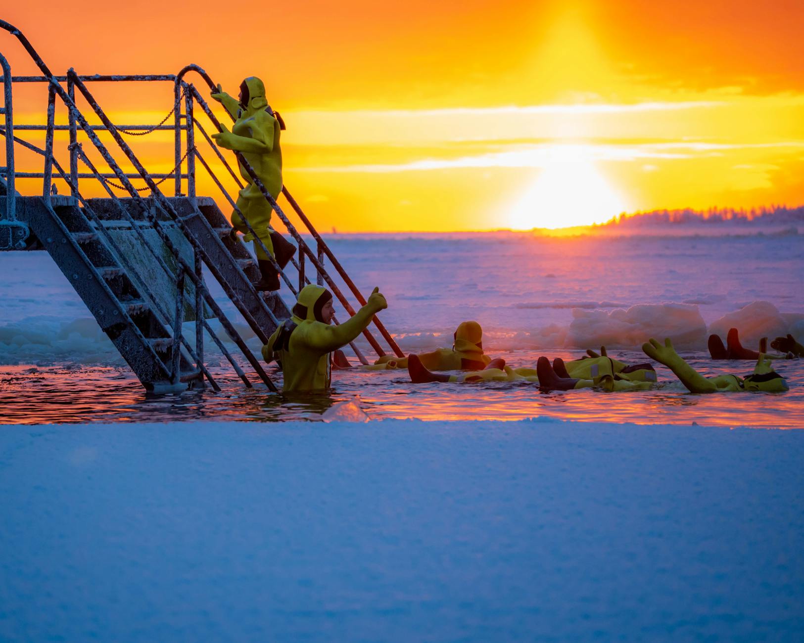 crioterapia sportiva — Group of people in yellow suits ice bathing at sunrise with vibrant sky.