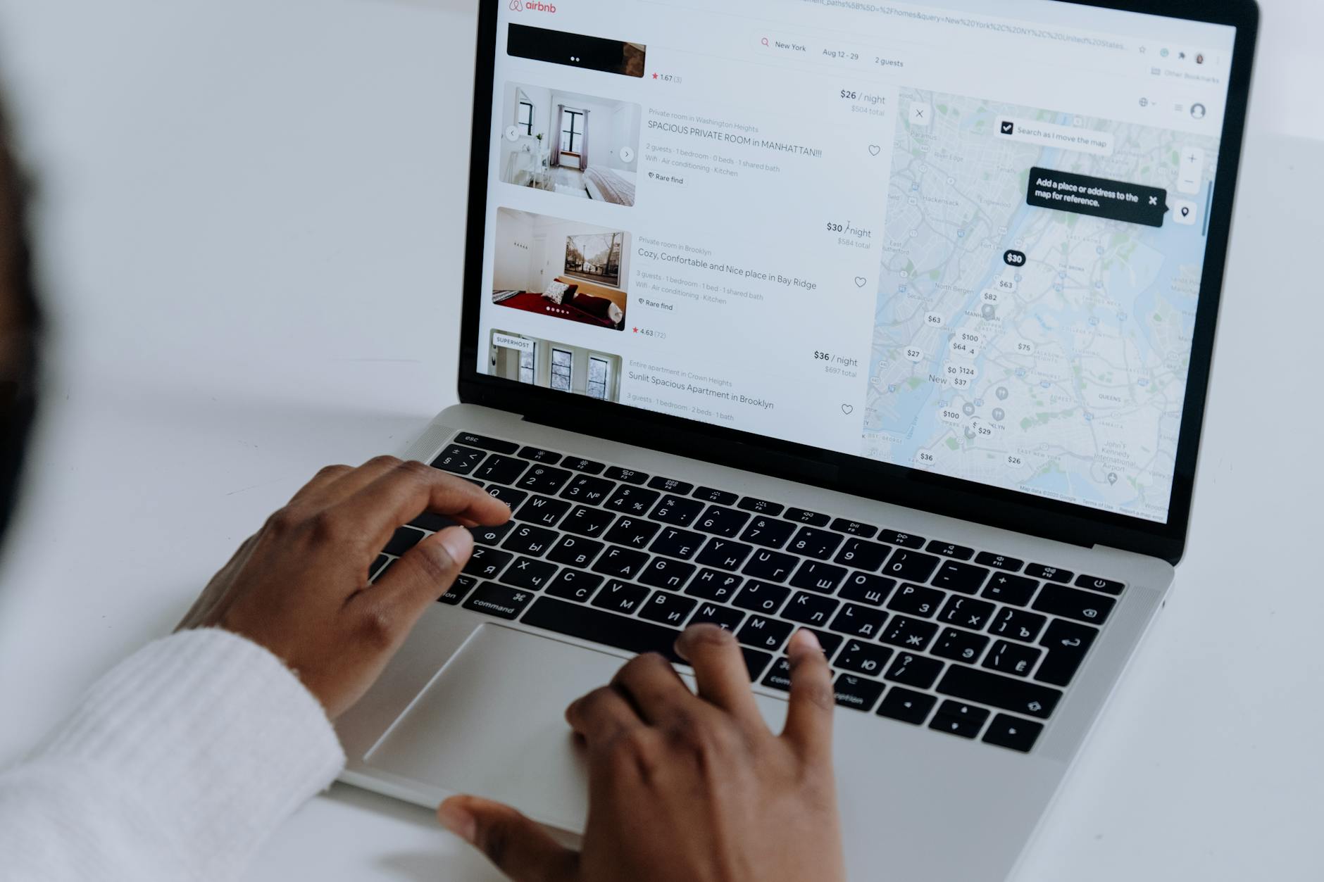 prenotare le vacanze — Hands typing on laptop searching Airbnb for accommodation options with map view.