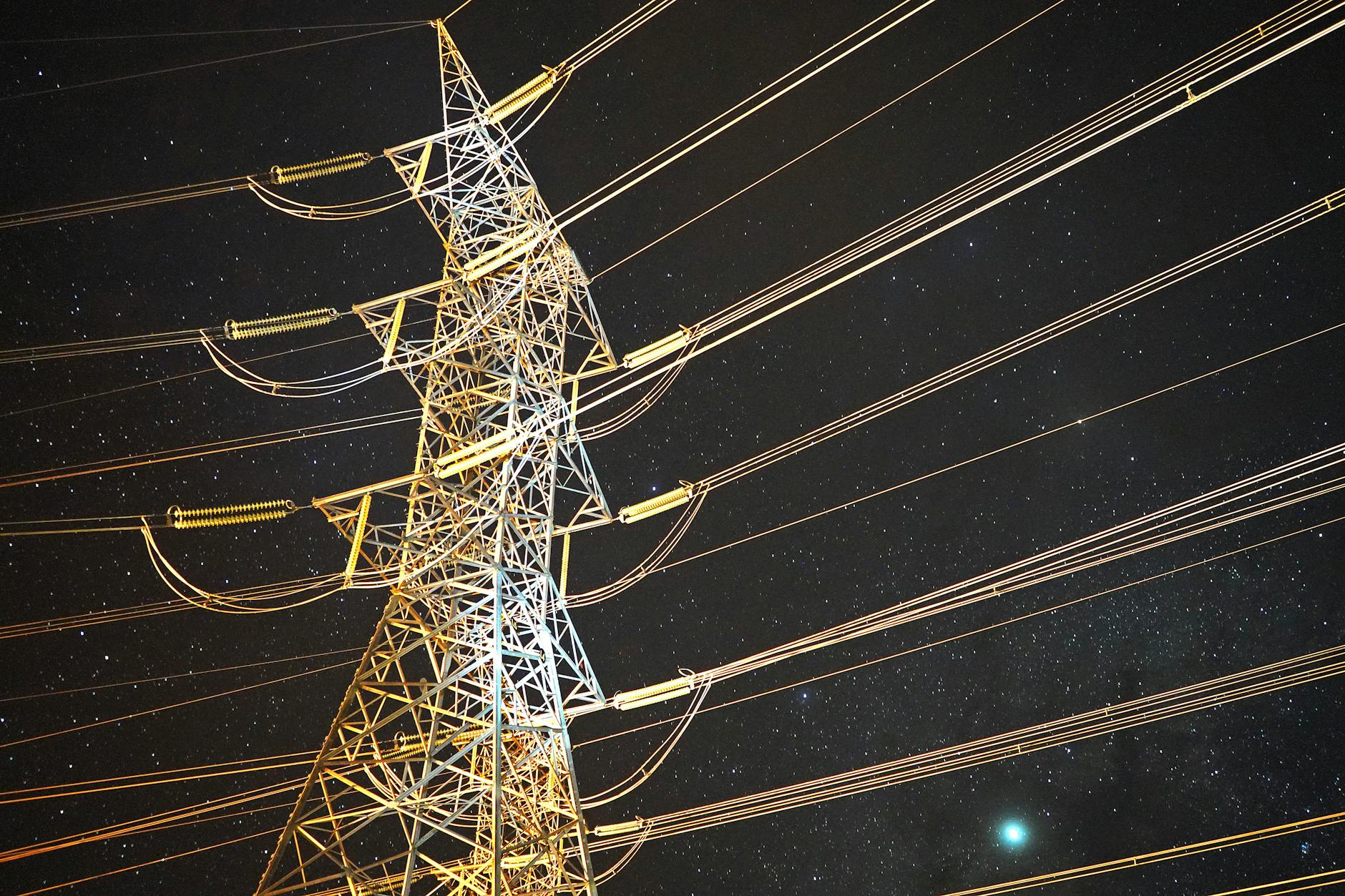 razionamento energetico — Illuminated power tower against a starry night sky, showcasing energy infrastructure.