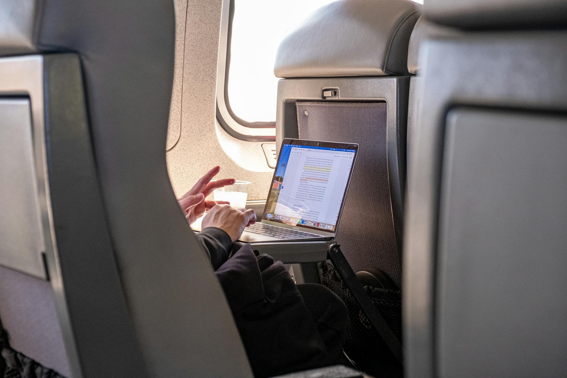servizi professionali viaggio — Passenger working on a laptop during flight, highlighting travel productivity.