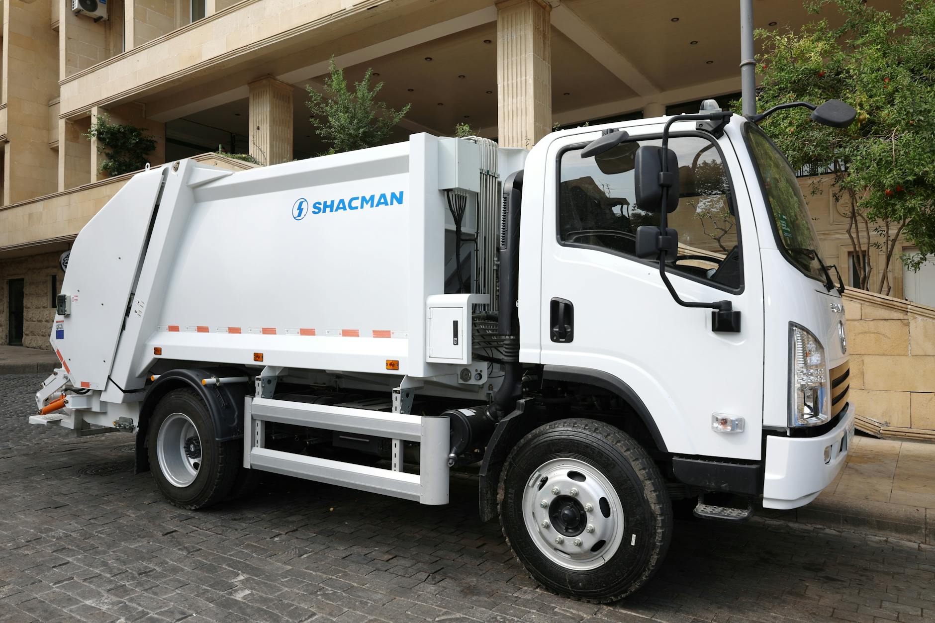 tariffe TARI 2026 — White Shacman garbage truck parked on a cobblestone street in an urban area, ready for waste collection.
