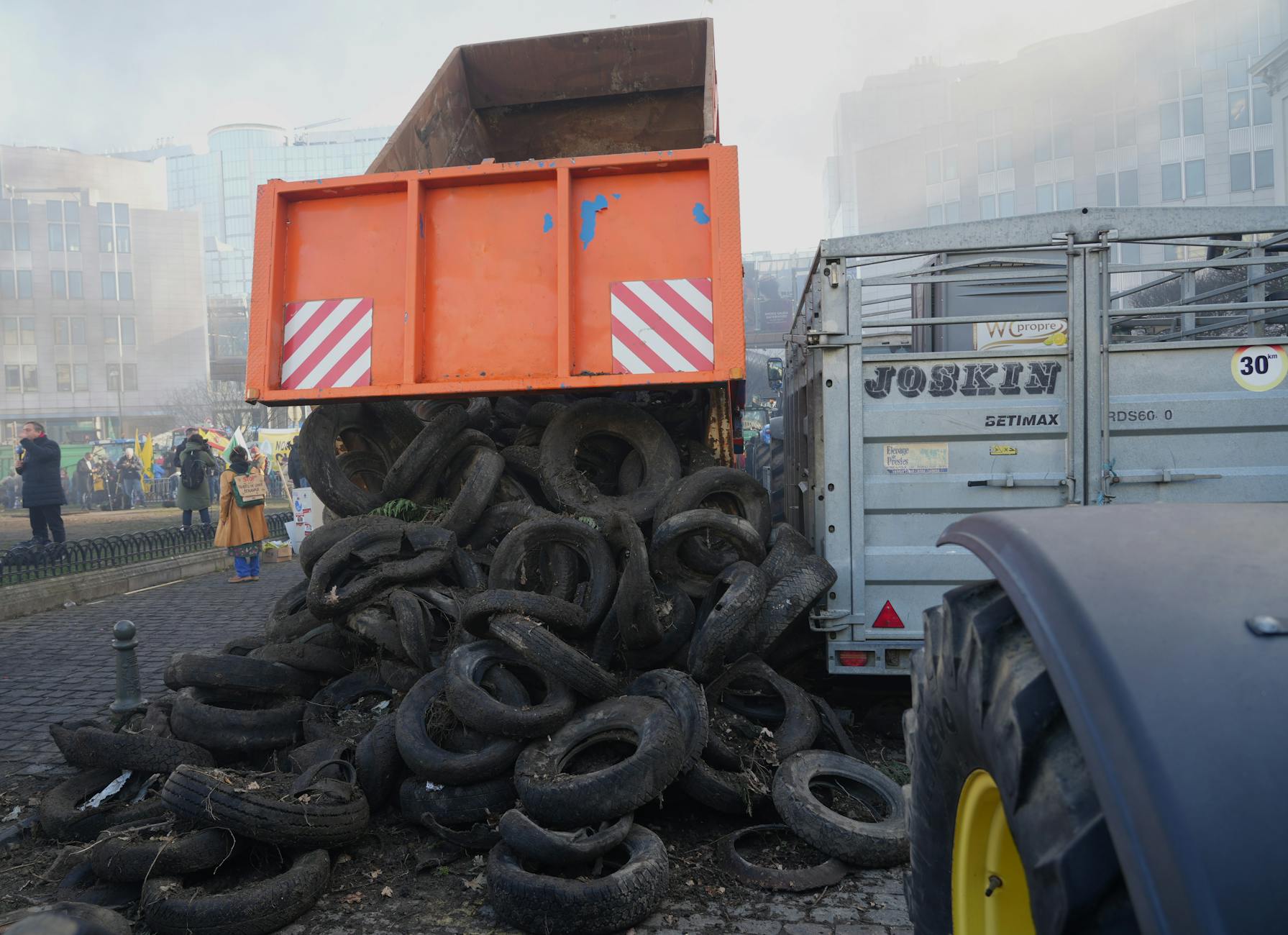 sciopero autotrasporti — Protest in city street featuring dump truck unloading tires, surrounded by people and buildings.