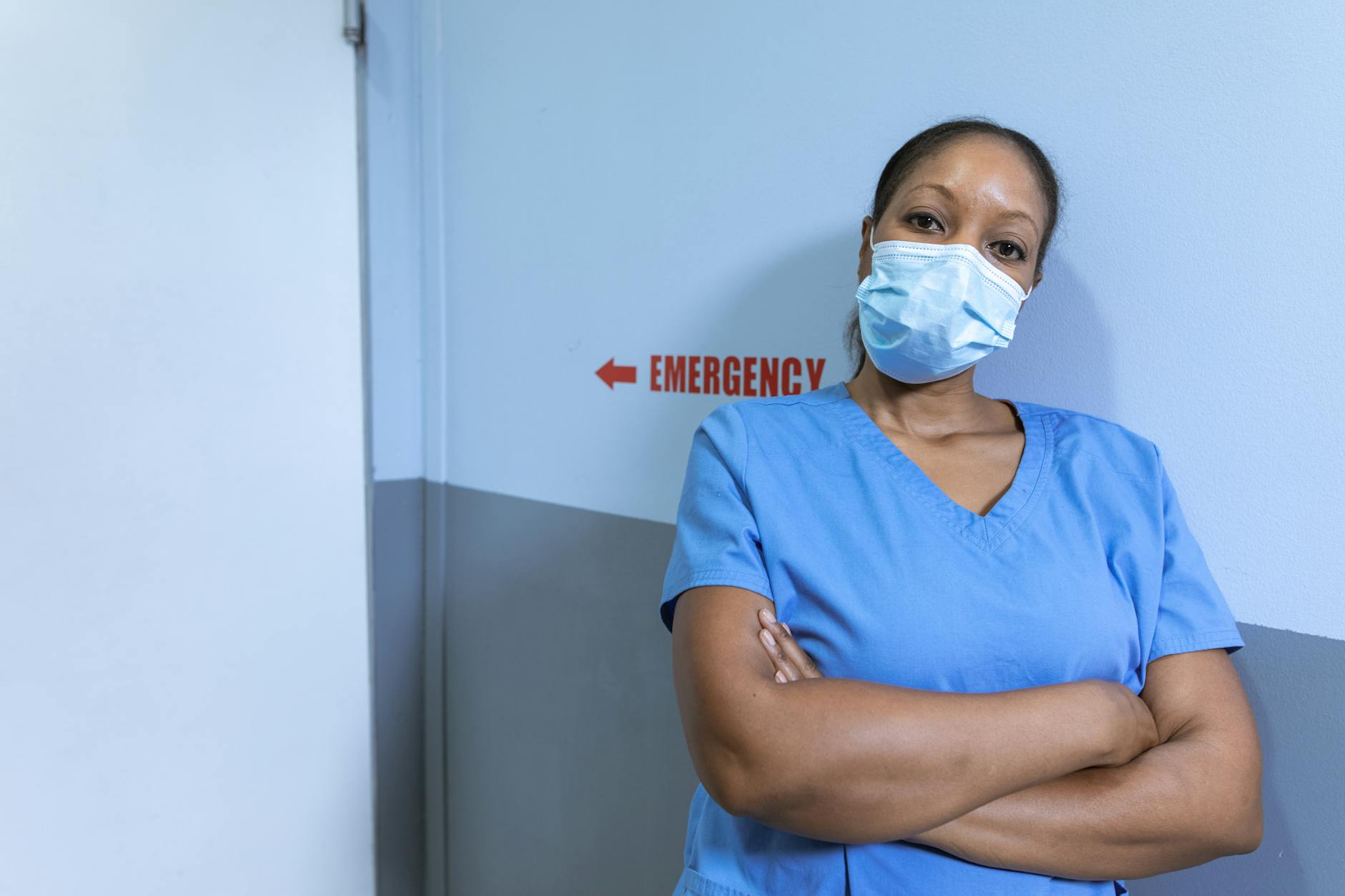 sciopero sanità privata — Nurse in blue scrubs and face mask in hospital corridor with emergency sign.