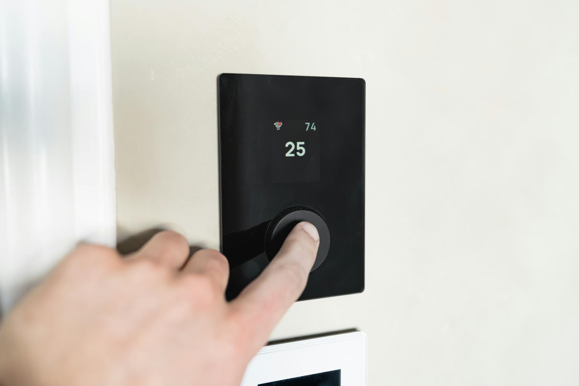 termostati smart — Close-up of a hand adjusting a sleek, modern smart thermostat on a wall.
