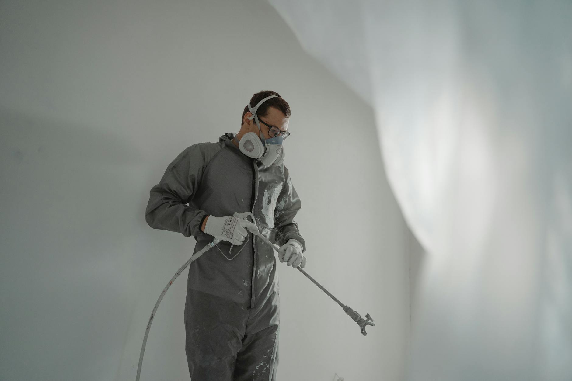 detrazioni fiscali tinteggiatura — Person in protective gear painting a wall, showcasing house renovation work.