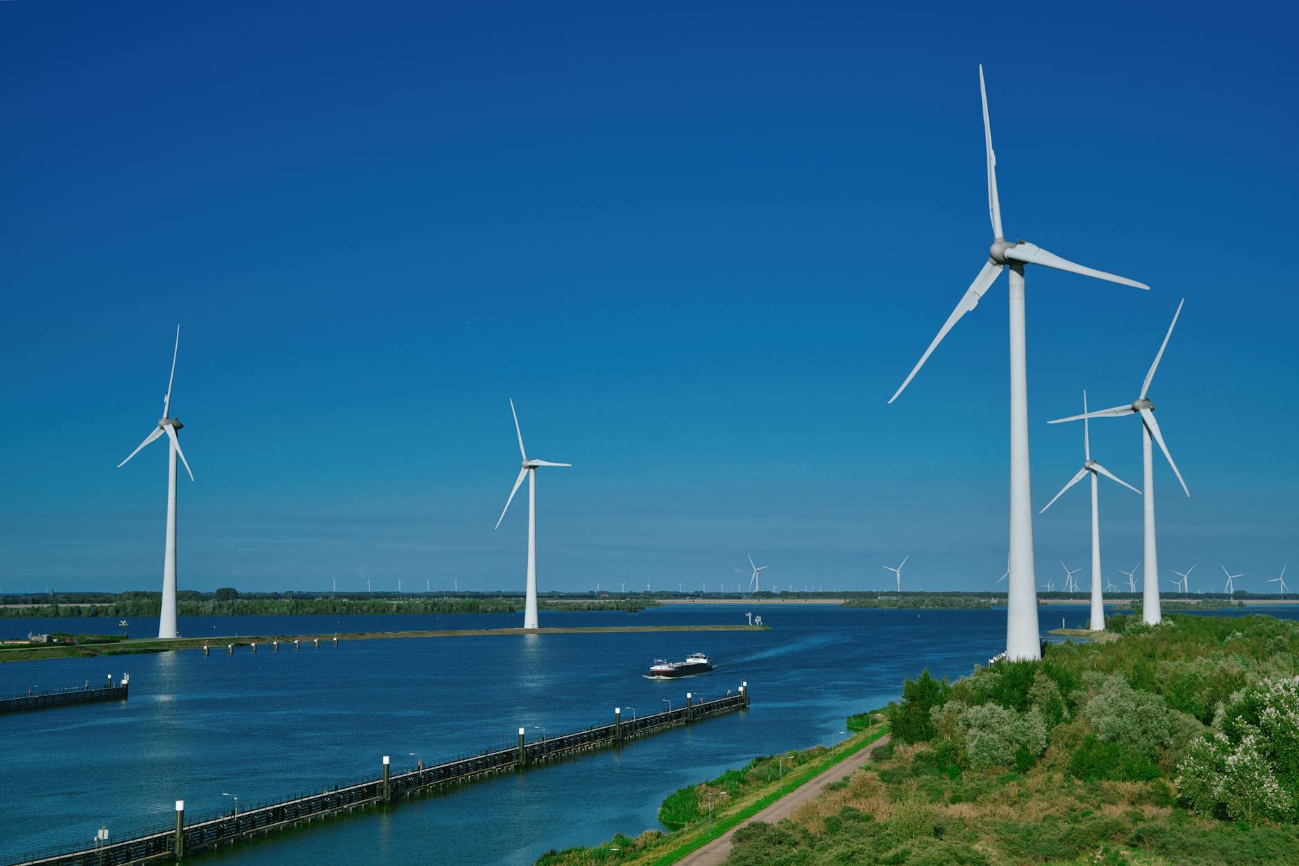 autonomia energetica europea — Renewable wind energy turbines standing over water under a clear blue sky in Bruinisse.