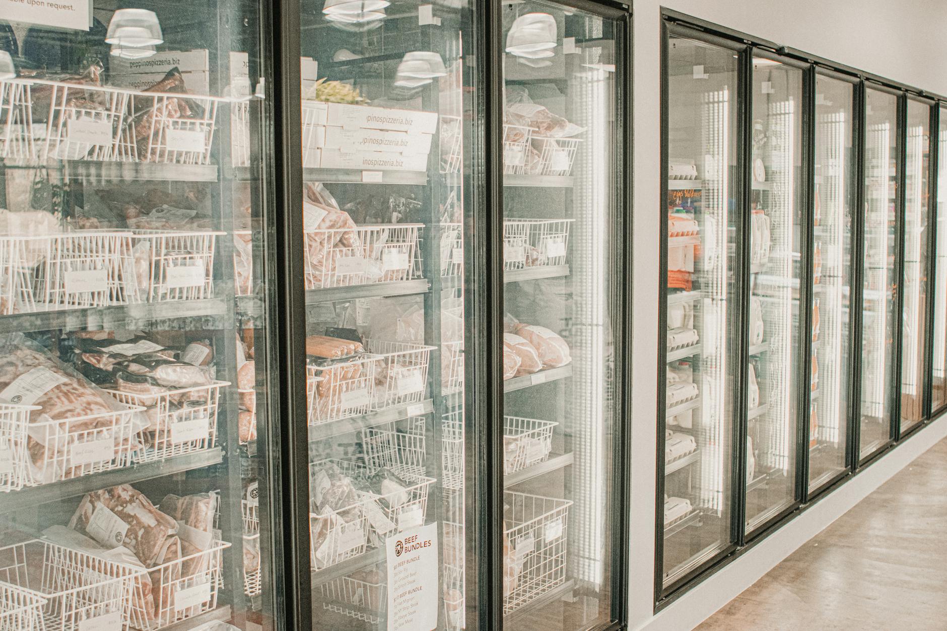 congelatori verticali 2026 — Frozen meats in a retail freezer with transparent doors and organized sections.