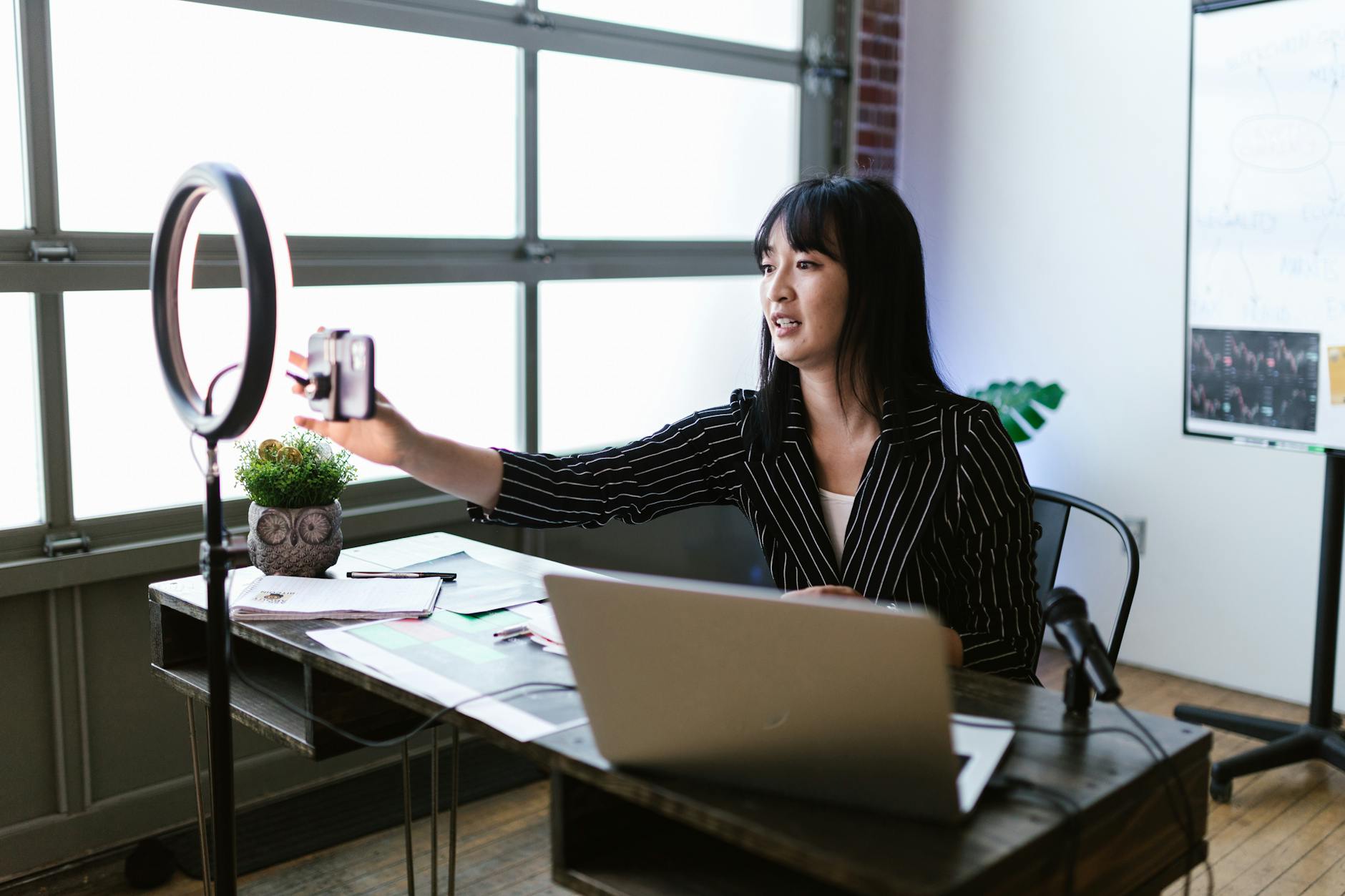 professionisti influencer — Woman using smartphone and ring light in office for content creation.