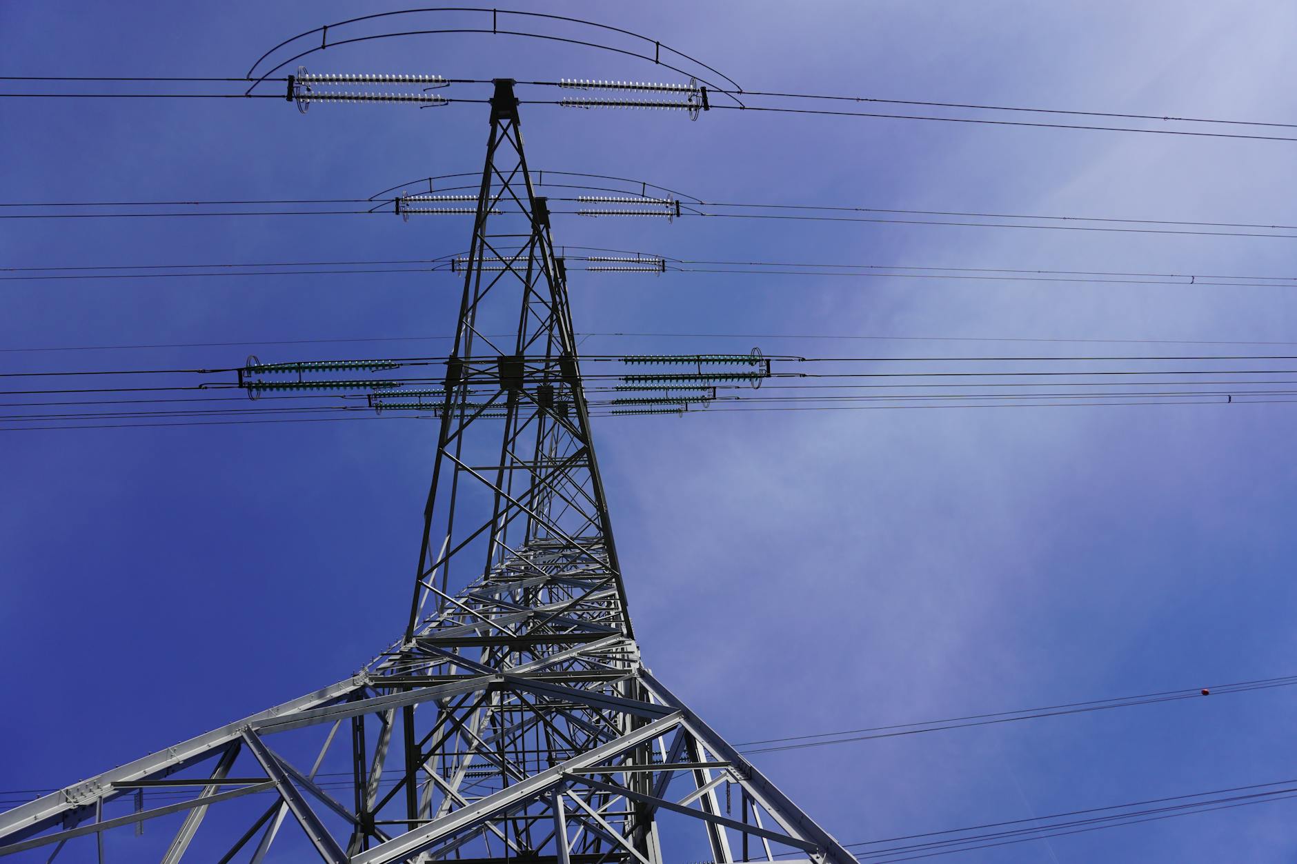 prezzo dell'energia elettrica — Steel electricity transmission tower against a clear blue sky, photographed from below.