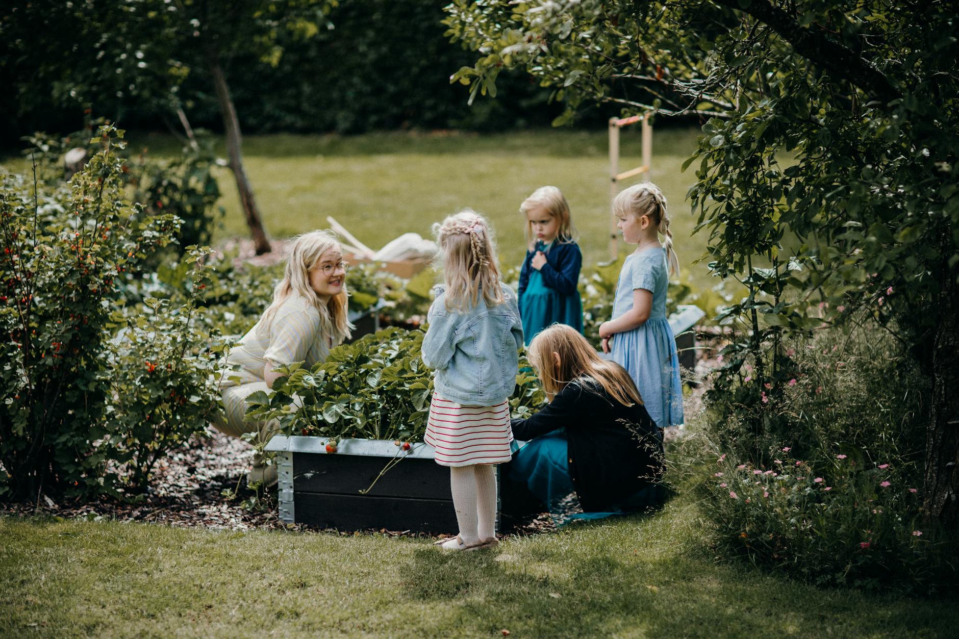 orto terapeutico Torino — A group of children and an adult gardening together in a lush, green backyard setting, enjoying outdoor activities.