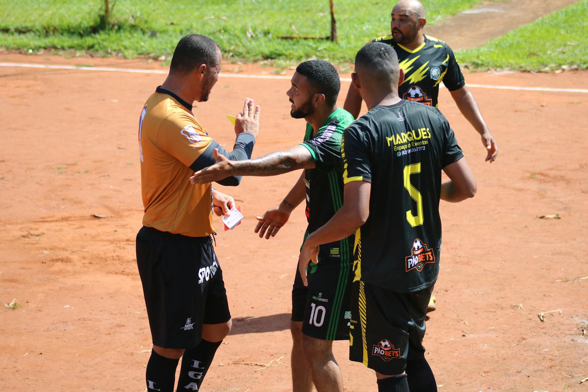 cartellino rosso diretto — A heated moment on the field as a referee shows a card to a player during a sunny soccer match.