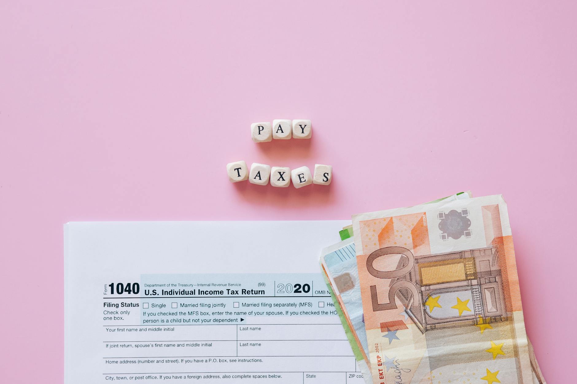 patrimonio estero italiani — Top view of tax form, euro banknotes, and 'Pay Taxes' letter blocks on pink background.