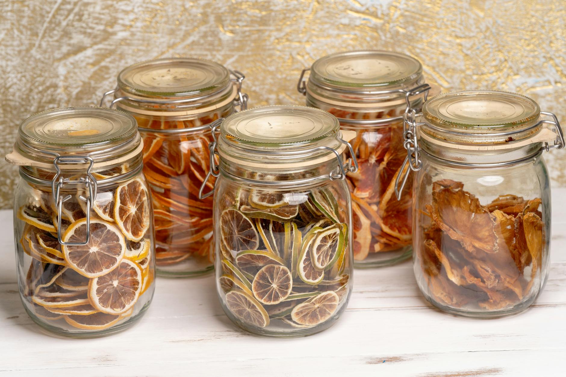 essiccatori domestici — Colorful, preserved dried fruits arranged neatly in decorative glass jars on a white surface.