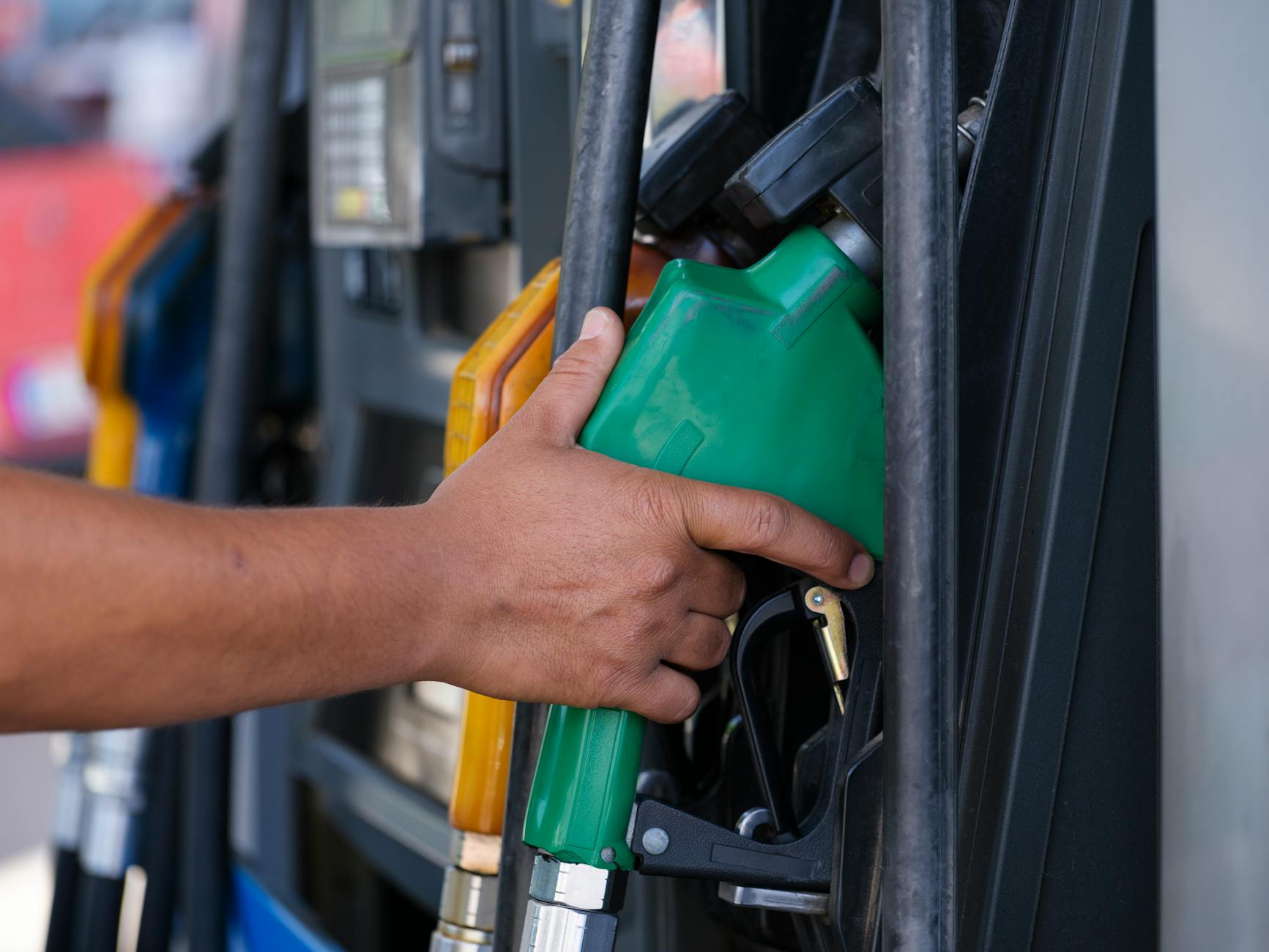 aumenti carburanti — Close-up of a hand holding a green fuel nozzle at a gas pump station outdoors.