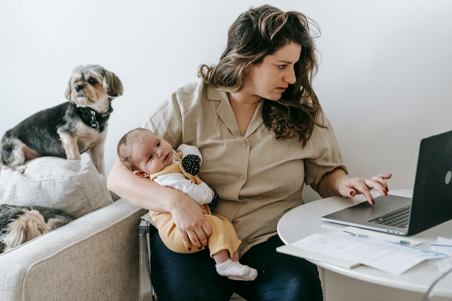 occupazione femminile — Mother balancing work from home with parenting, holding baby and typing on laptop.