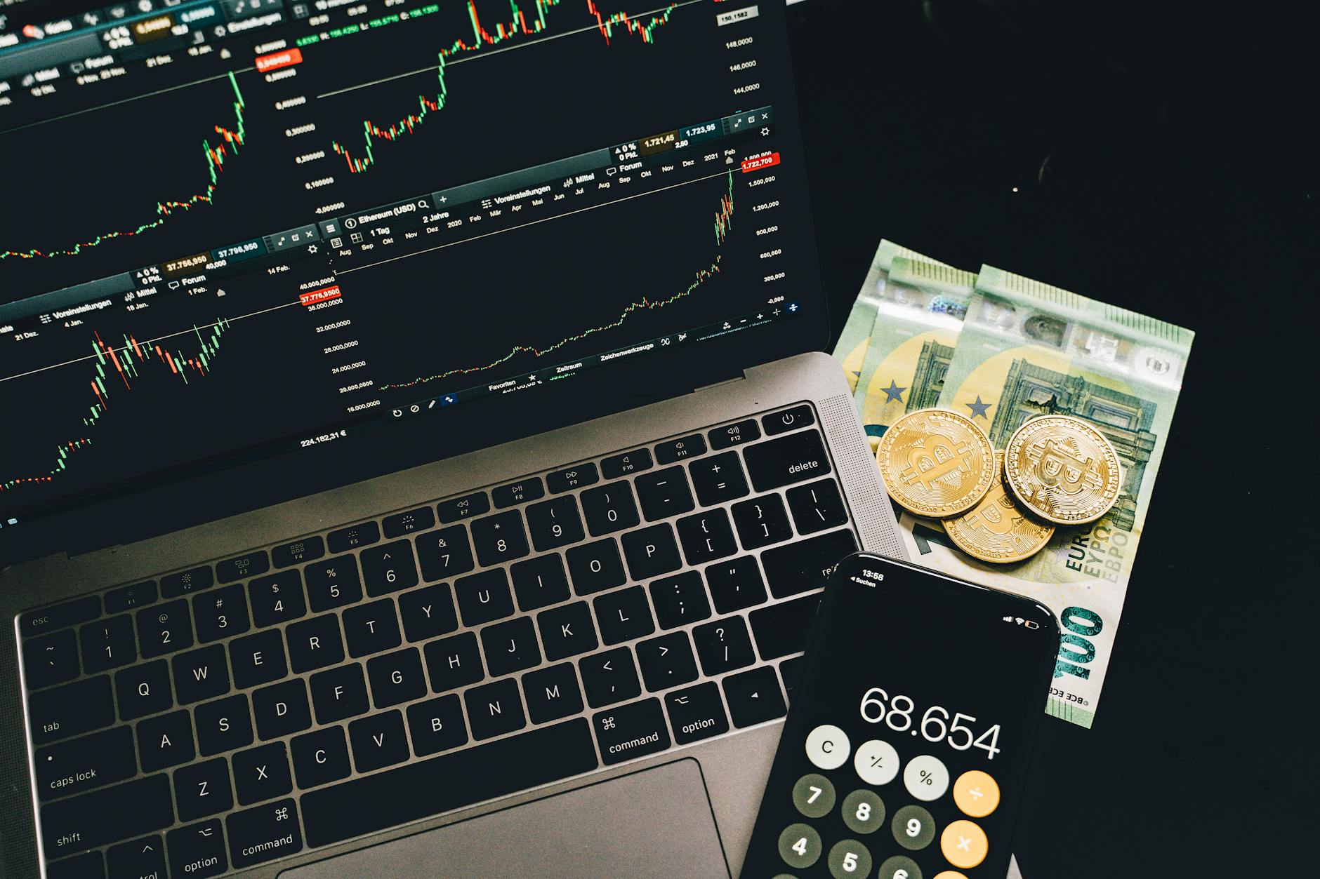 criptovalute geopolitica — A laptop displaying stock charts with Bitcoin, Euros, and a cellphone calculator, showcasing financial analysis.