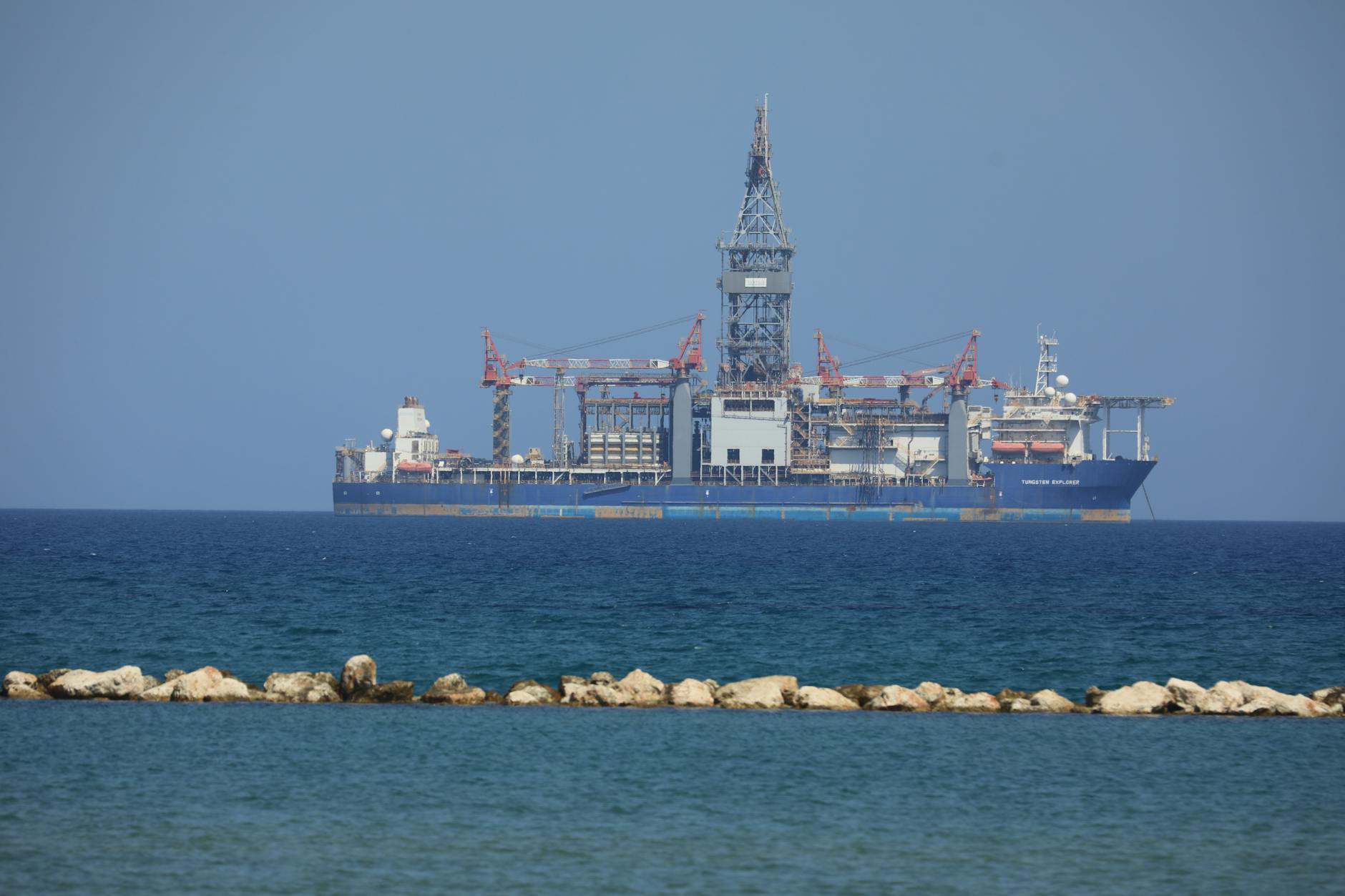 petrolio Brent — An offshore drilling rig floats on a calm sea with a clear blue sky in the background.