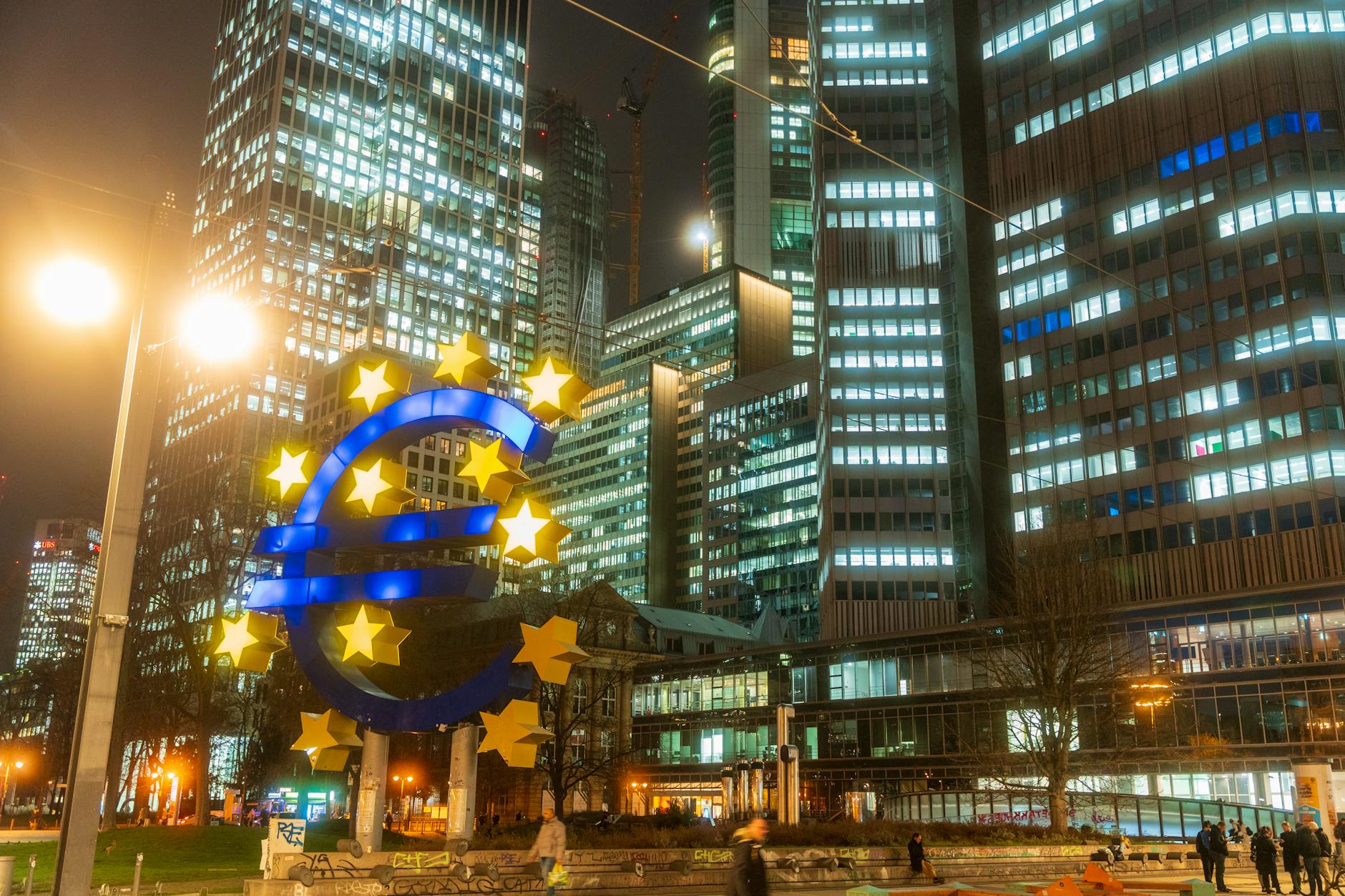rischi economici BCE — Night view of the iconic Euro sculpture in Frankfurt's bustling financial district.