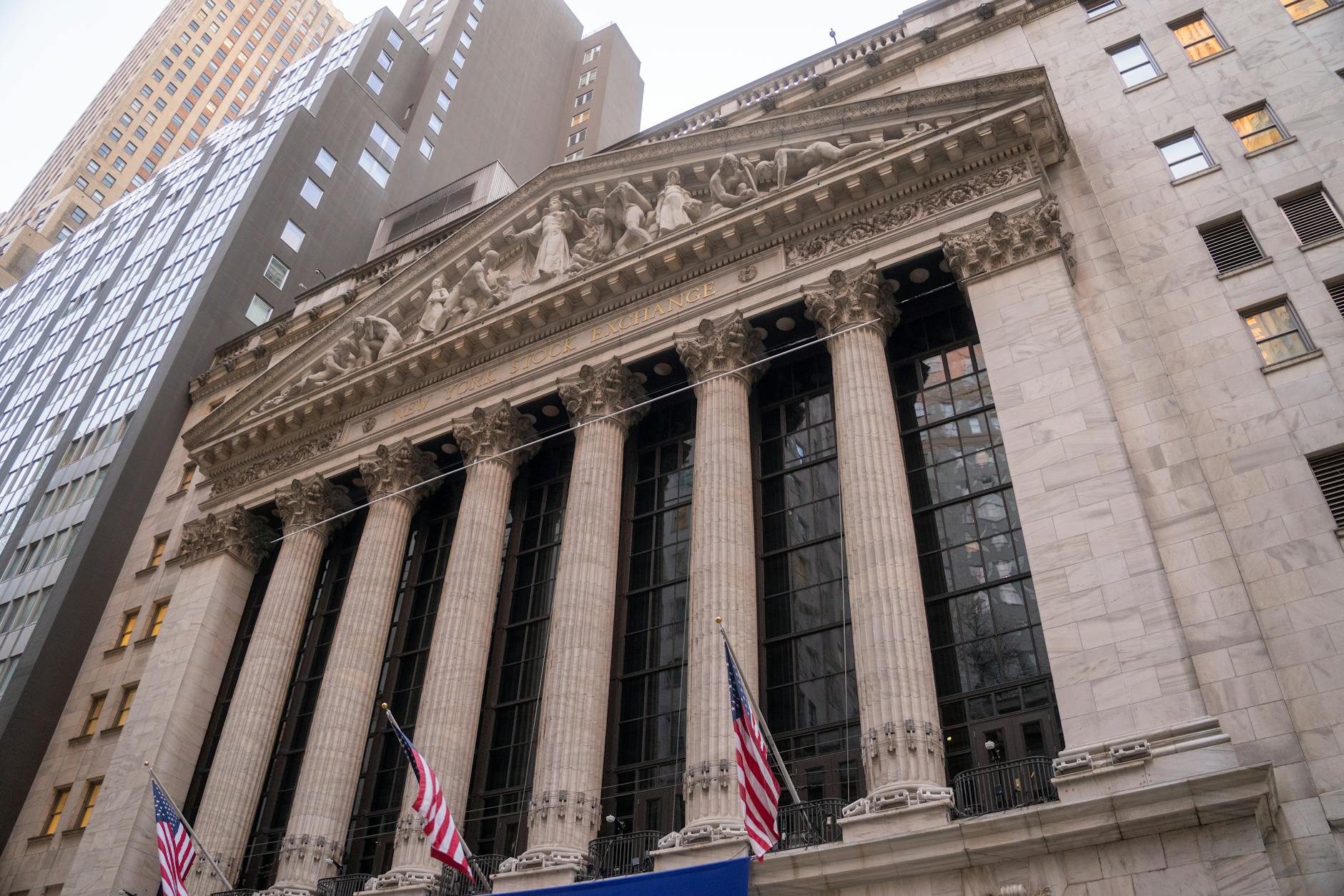 mercati finanziari americani — Close-up view of the iconic New York Stock Exchange building with American flags, located in Wall Street, NYC.