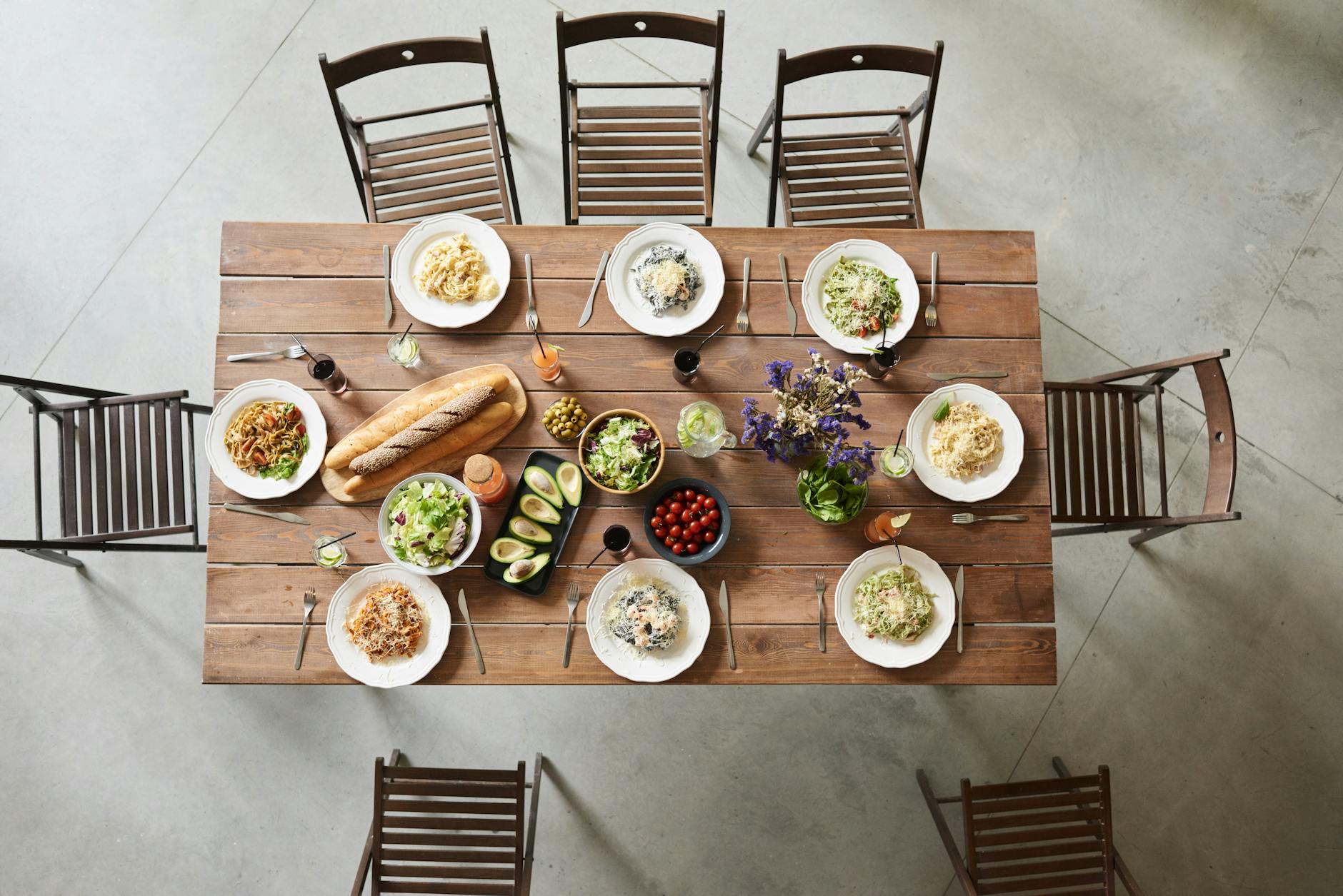 convivialità italiana — Top view of a wooden table set with pasta dishes, fresh ingredients, and drinks for a cozy meal.