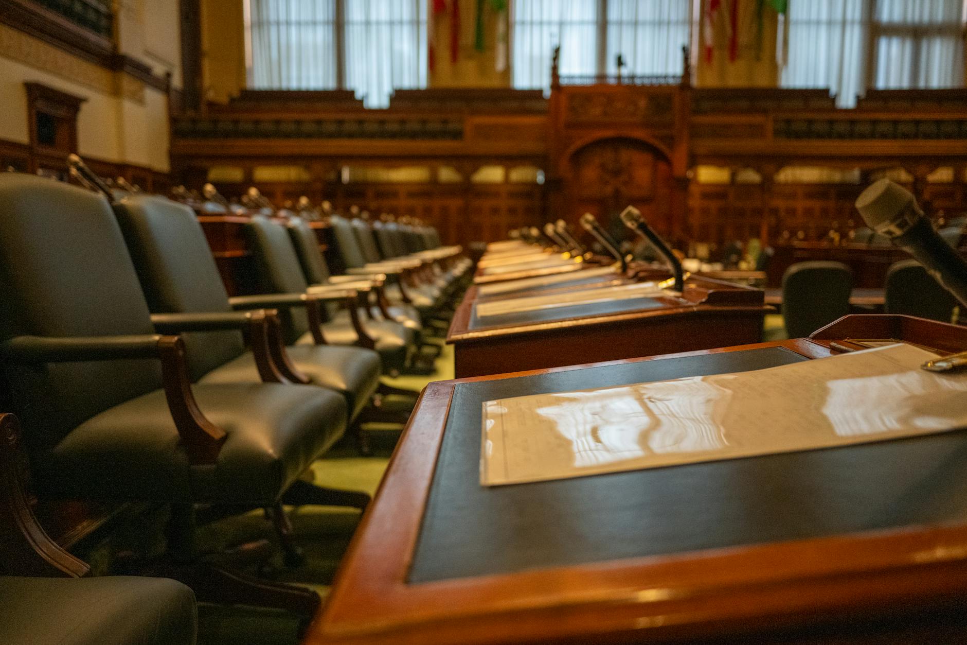 manovra correttiva — A detailed view of an empty legislative chamber with rows of desks and microphones, evoking governance.
