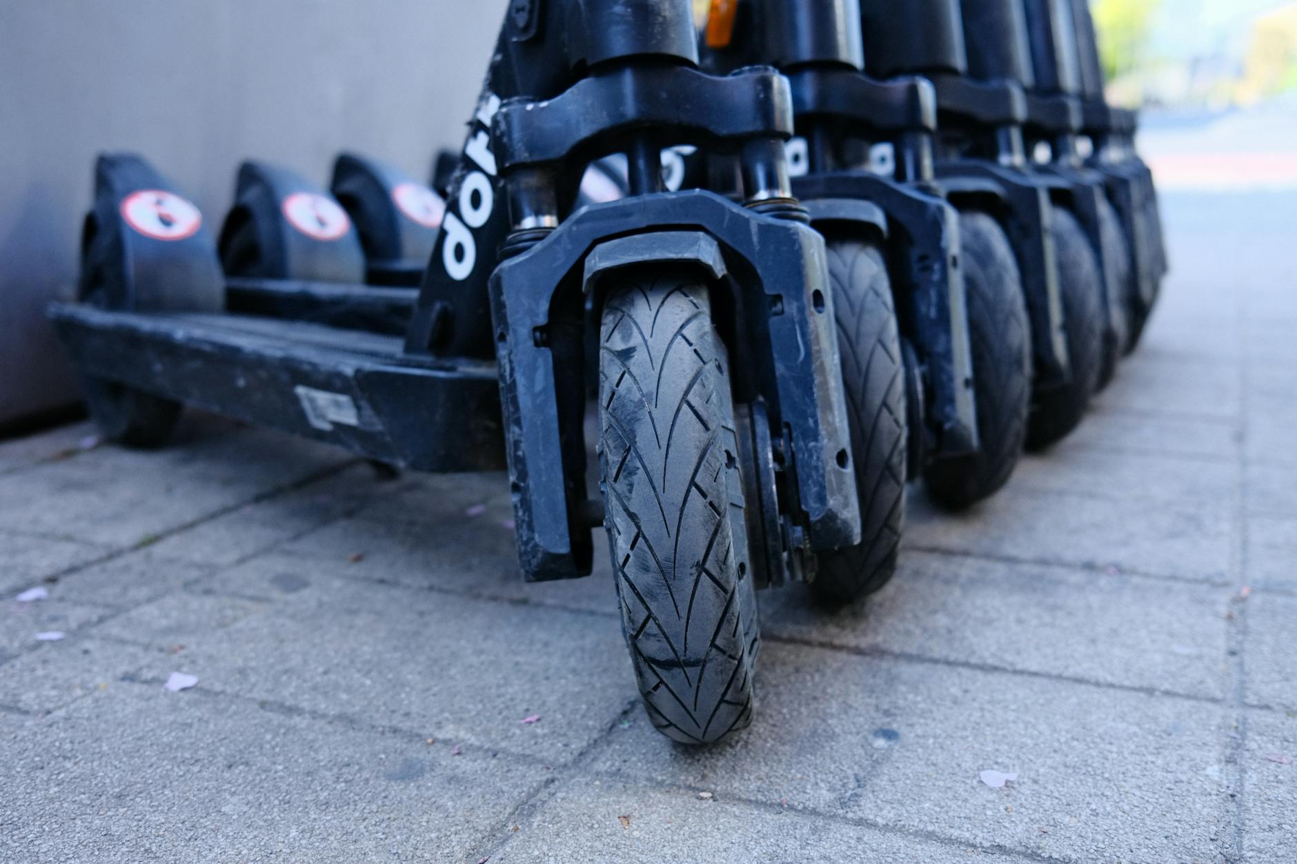 obbligo targa monopattini — Row of parked electric scooters on a city sidewalk, focusing on wheels.