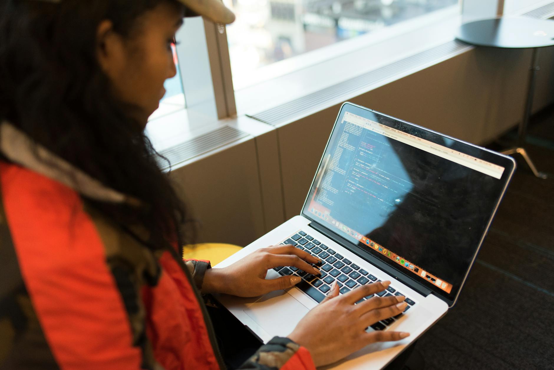 divario tecnologico genere — A focused woman typing code on her laptop indoors, embodying tech innovation.
