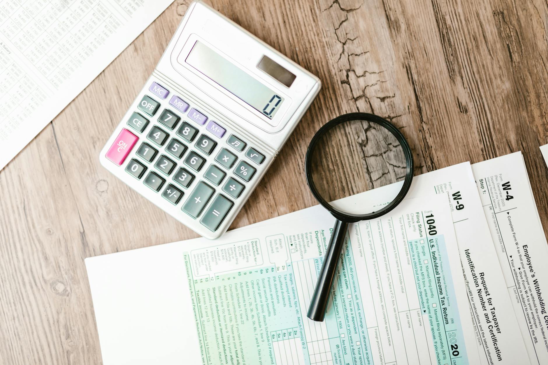 riforma fiscale — Tax forms laid out with a calculator and magnifying glass on a wooden surface, perfect for finance themes.