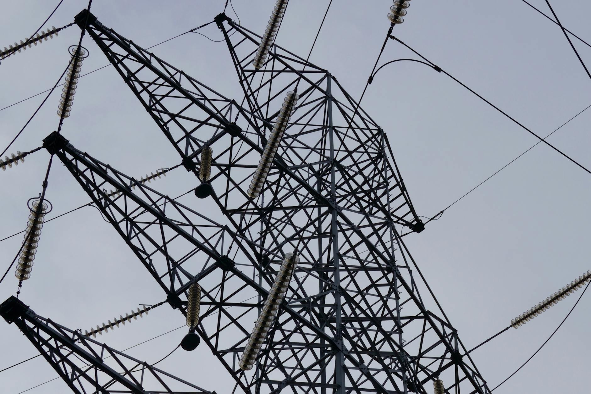 clausola di salvaguardia energia — Low angle shot of a metal power transmission tower with cables against a clear sky.
