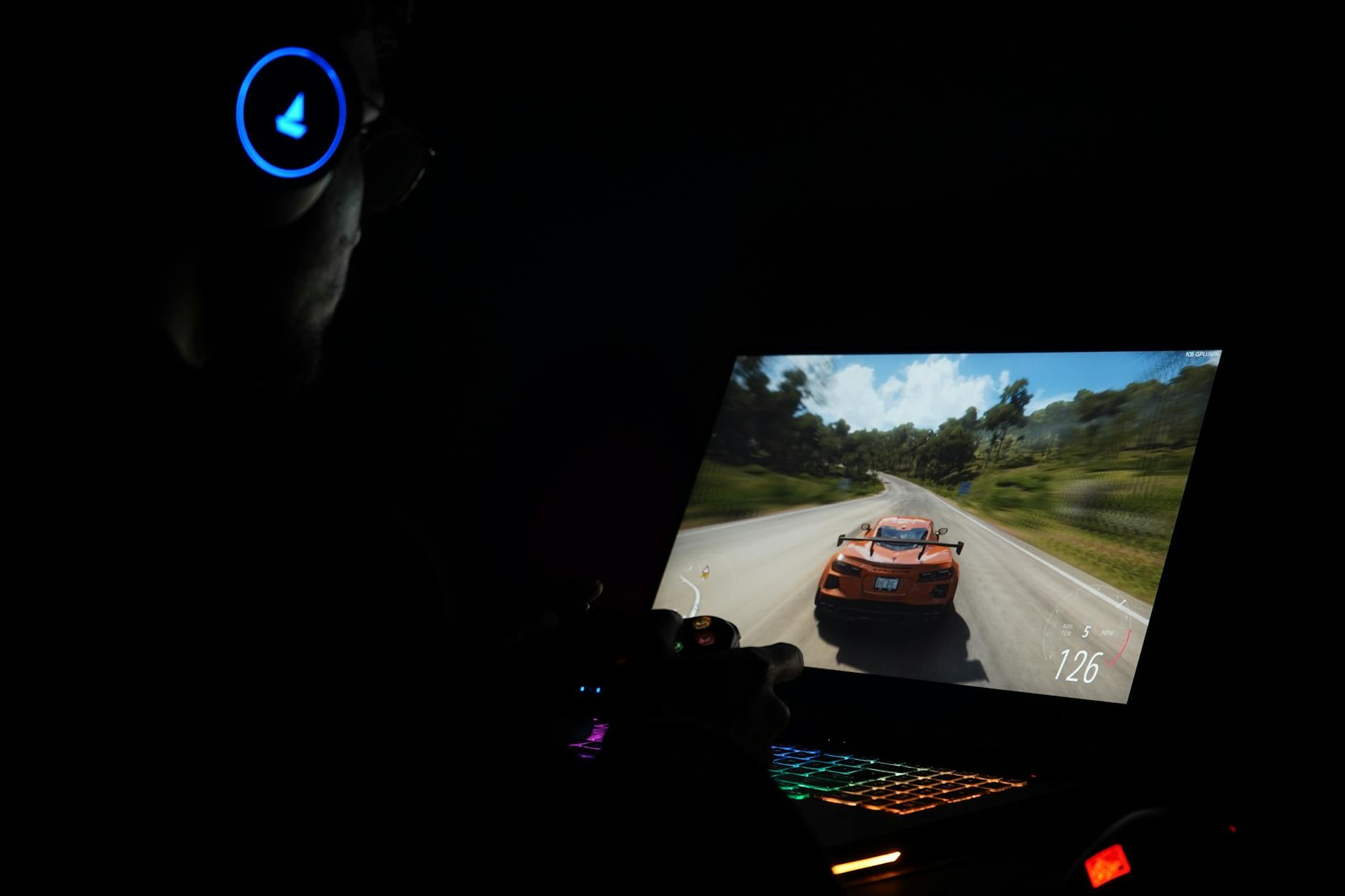 videogiochi racing open world — A gamer using a laptop and headphones to play a car racing game in a dark setting.