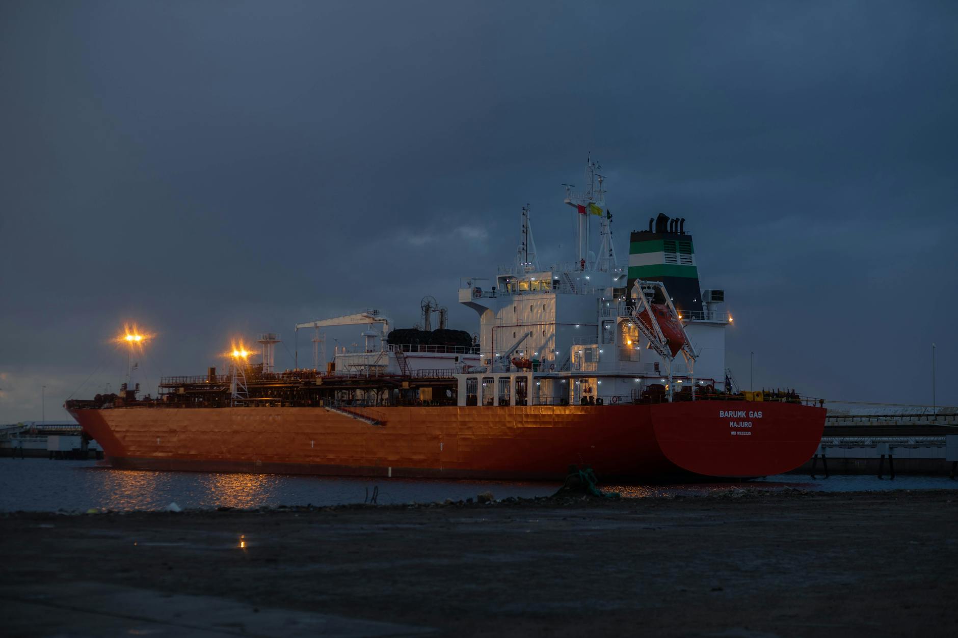 flussi petroliferi Hormuz — A large oil tanker ship illuminated at night, docked at a harbor.