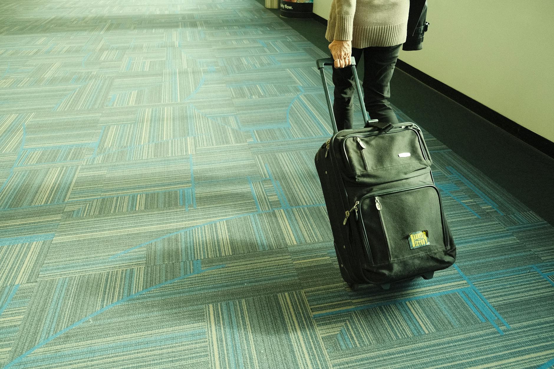 sentenza bagagli smarriti — Person walking with luggage on blue carpeted airport corridor, traveling